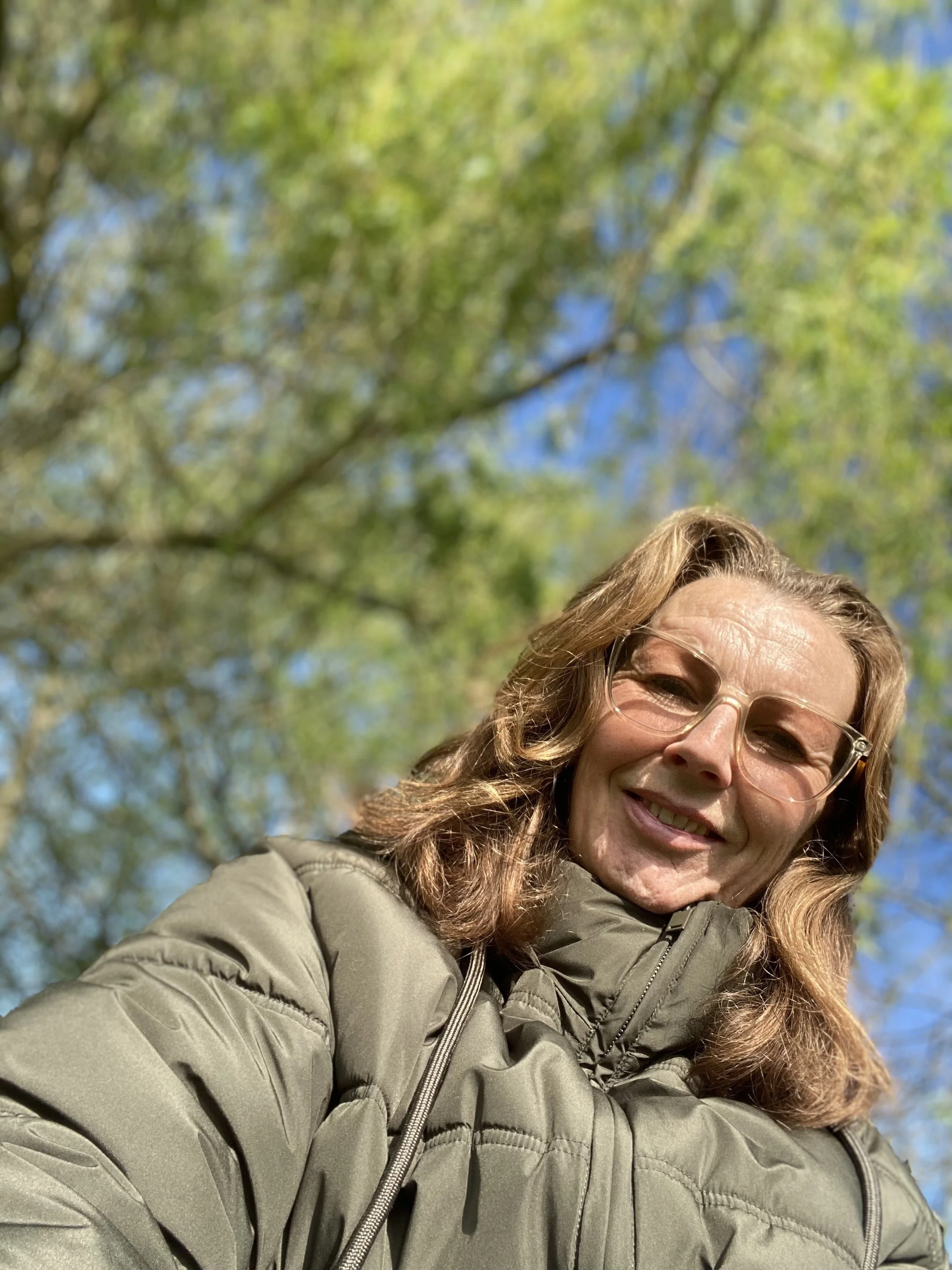 Louise outside wearing sunglasses with a background of blurred green trees and blue sky.