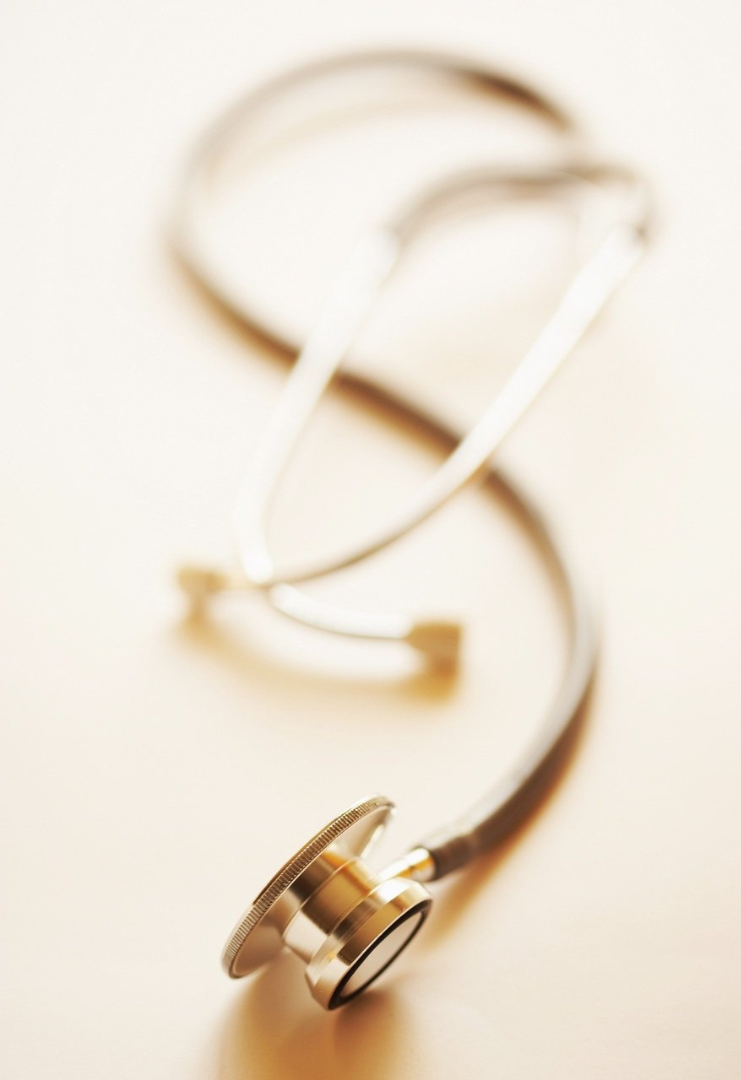 Close-up of a gold-colored stethoscope lying on a white surface, with the earpieces out of focus in the background.