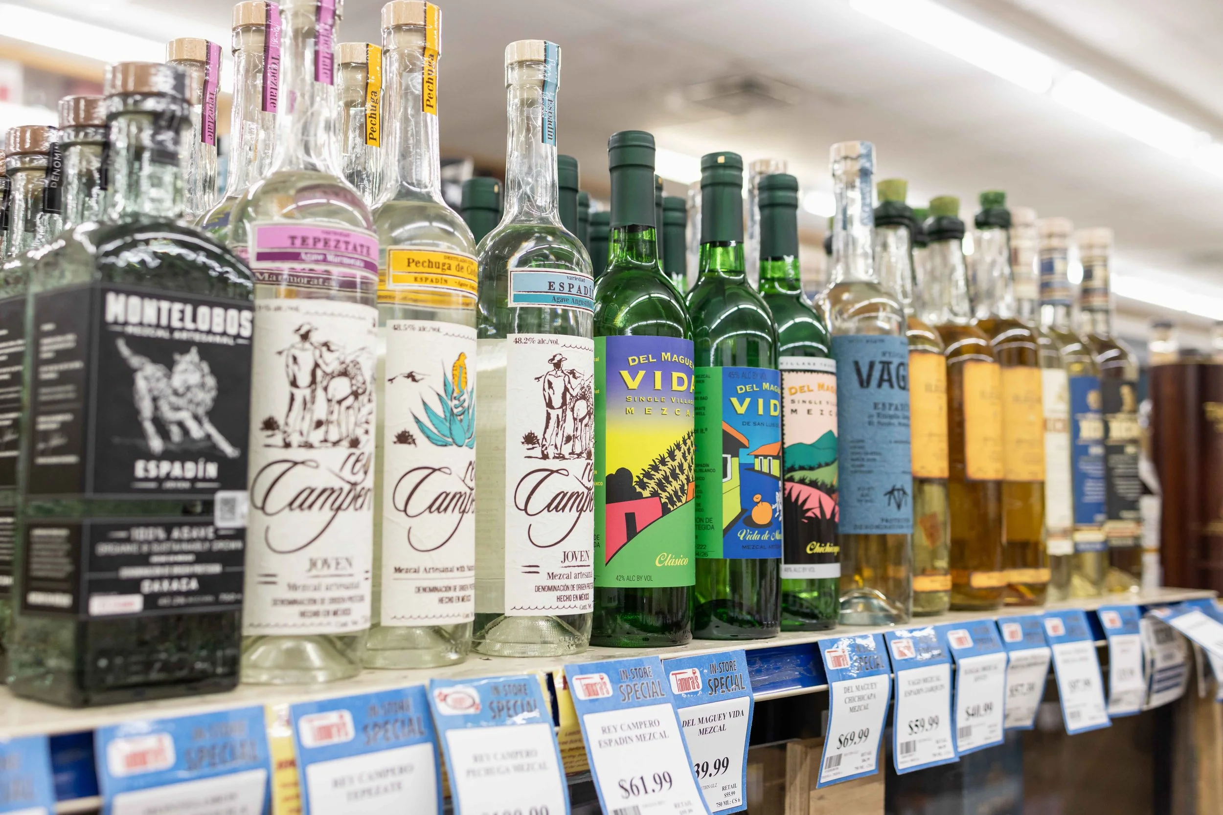 Various bottles of tequila on store shelves with price tags visible below.