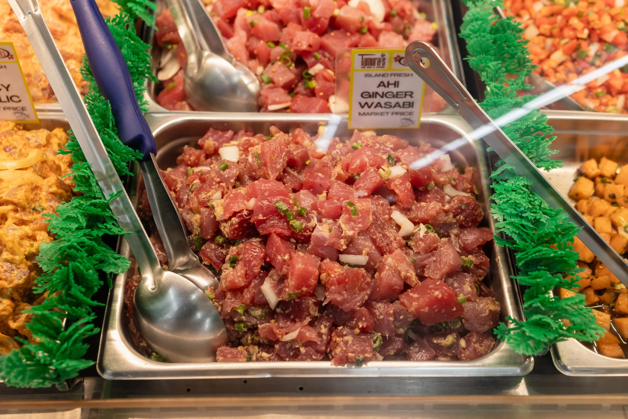 Tray of raw ahi tuna pieces garnished with chopped green onions at a seafood market. Labels indicate the variety as ginger wasabi.