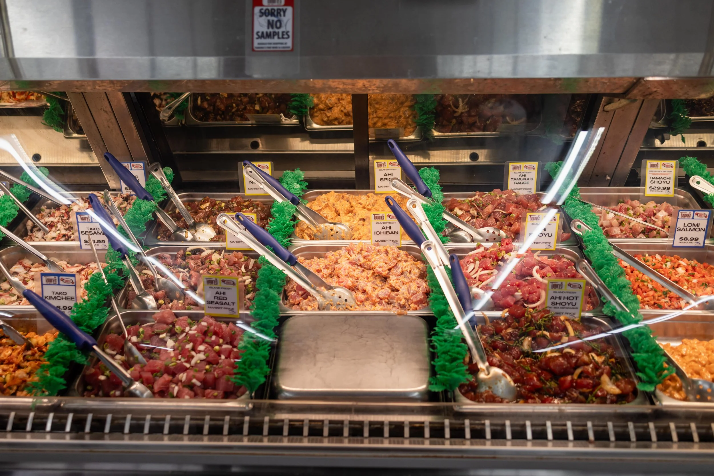 Assorted raw meats and seafood in a grocery store display case with labels and tongs.