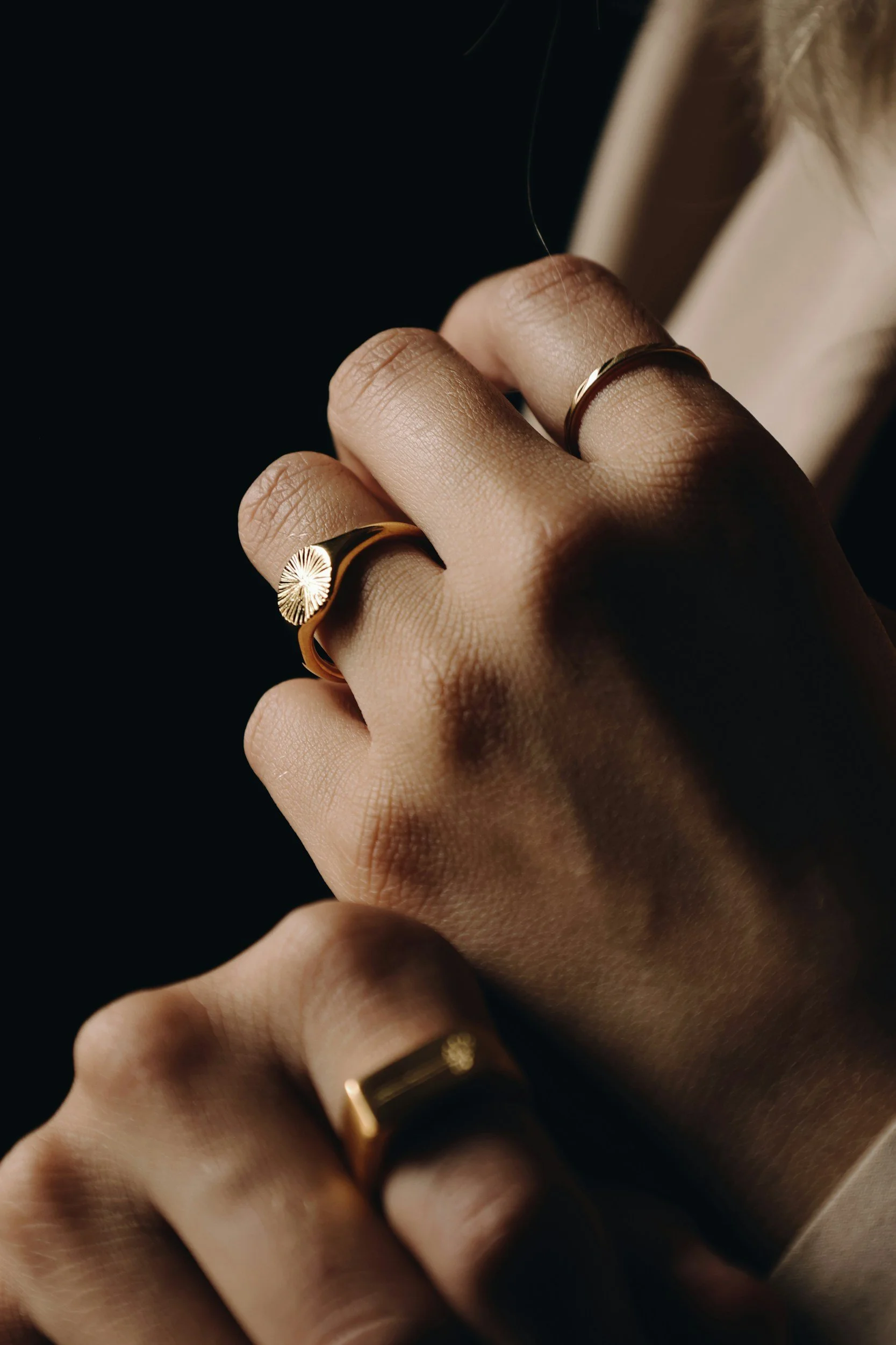 Close-up of a person's hand wearing multiple gold rings, with one featuring a sunburst design, against a dark background.