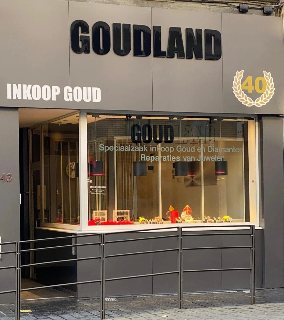 Winkelpand met de naam Goudland, gespecialiseerd in inkoop, diamant en reparatie van sieraden. Er is een grote raamtoonbank met sieraden en decoraties in de etalage, en boven het raam een bord met de teksten 'Goudland' en 'Inkoop Goud'. Een gouden lauwerkrans met de tekst '40' is te zien rechtsboven.