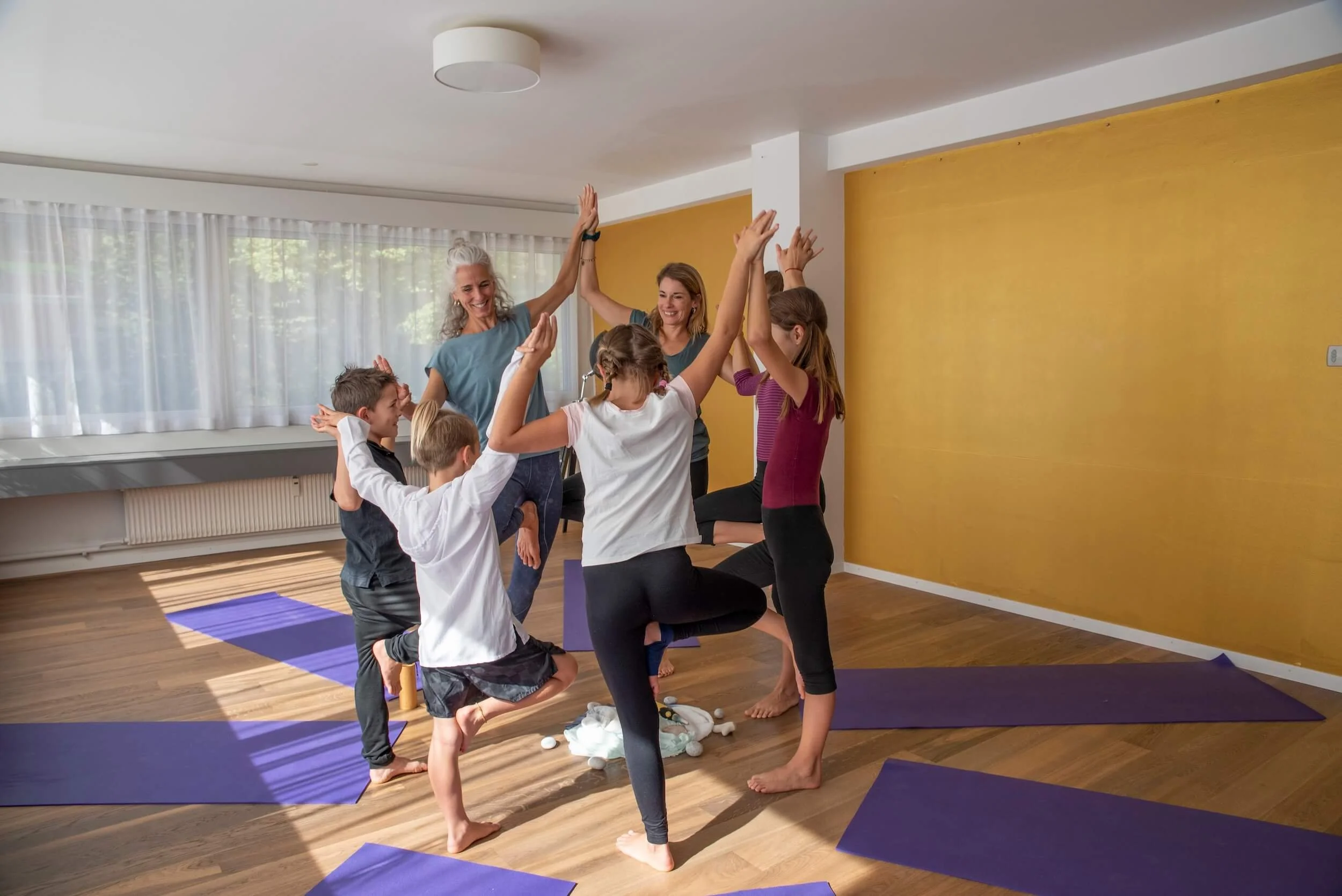Kinder, die Yoga in einem Raum in Bern mit Glasfenstern und einer gelben Wand üben.