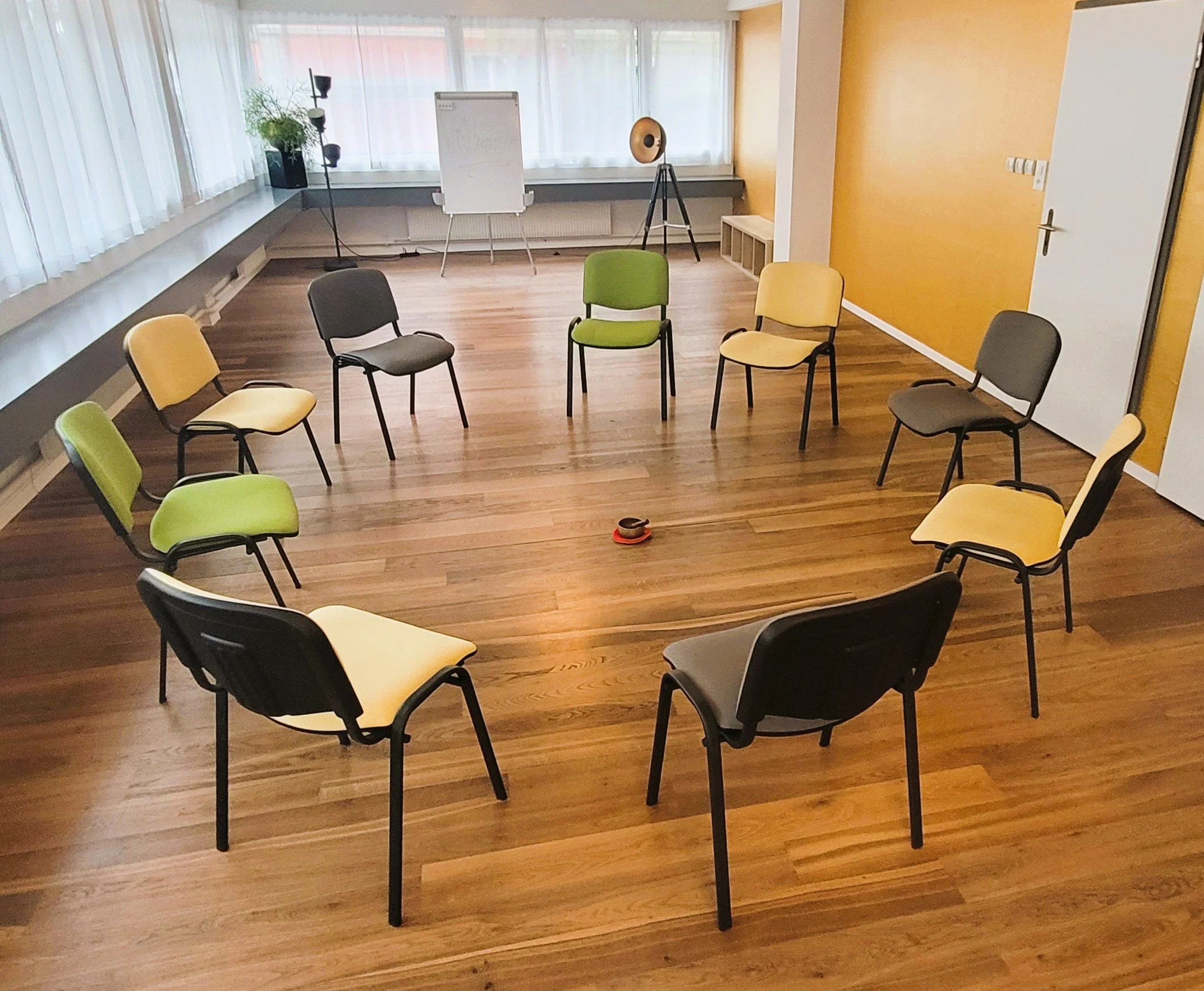 Ein Raum mit Stühlen in einem Kreis, einem Whiteboard, Pflanzen und Tontechnik, für einen Workshop oder eine Sitzung, mit großen Fenstern und Holzboden in der Länggasse in Bern.