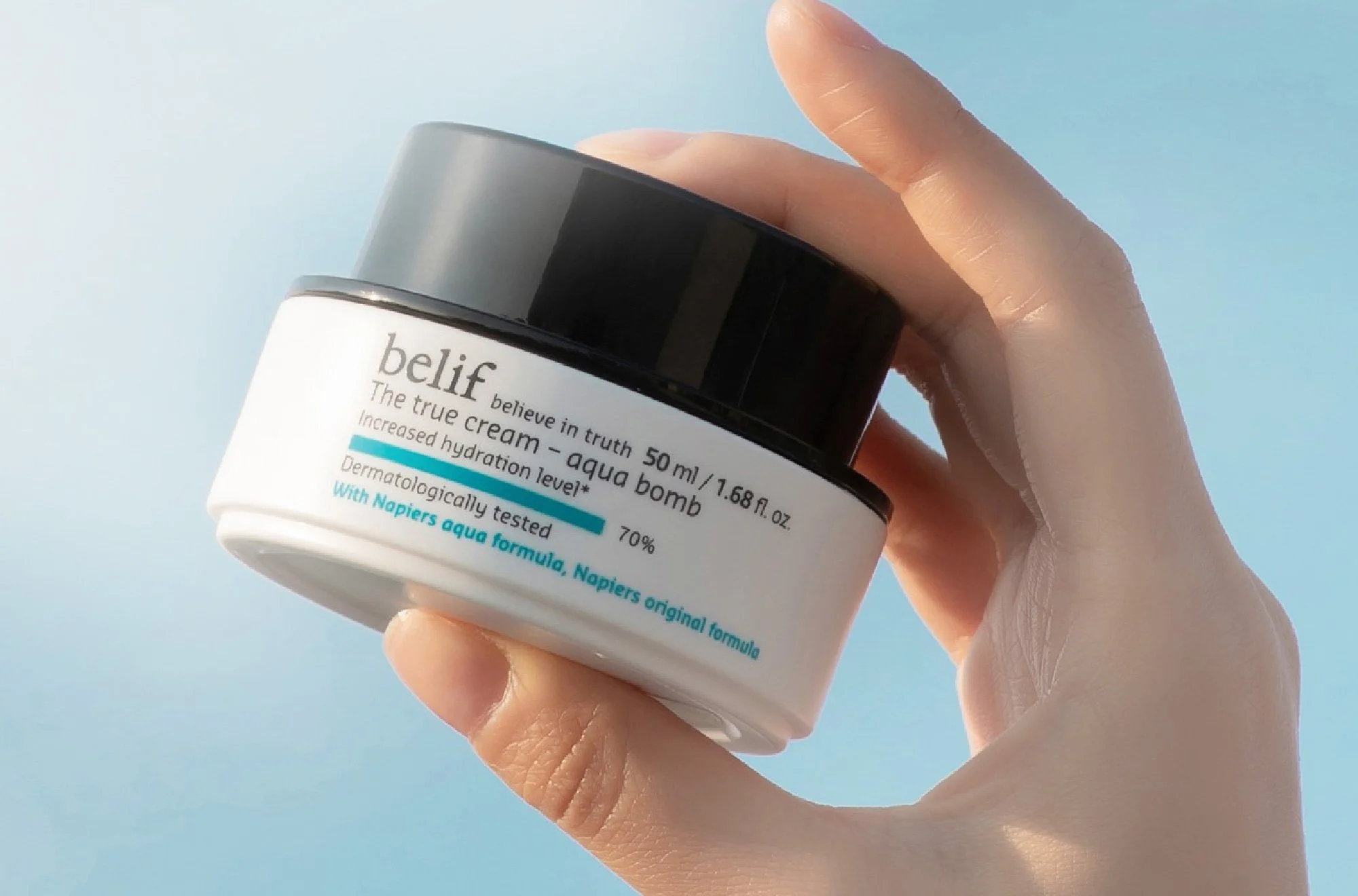 A hand holding a small green bottle of skincare serum with a dropper cap.