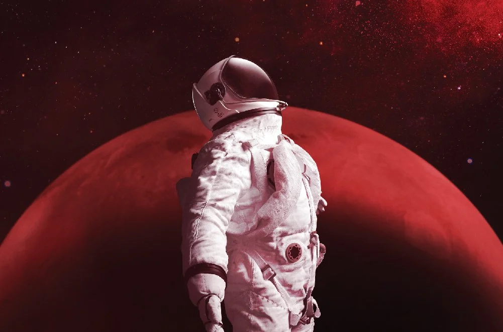 An astronaut in a white space suit standing in front of a large red planet against a dark starry background.