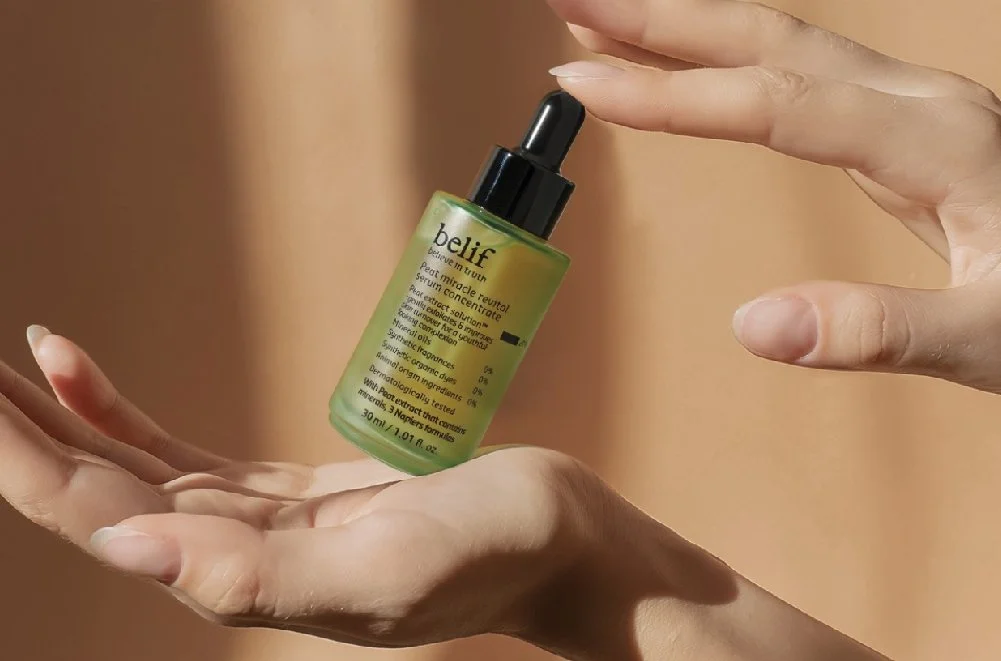 A hand holding a small green bottle of skincare serum with a dropper cap.