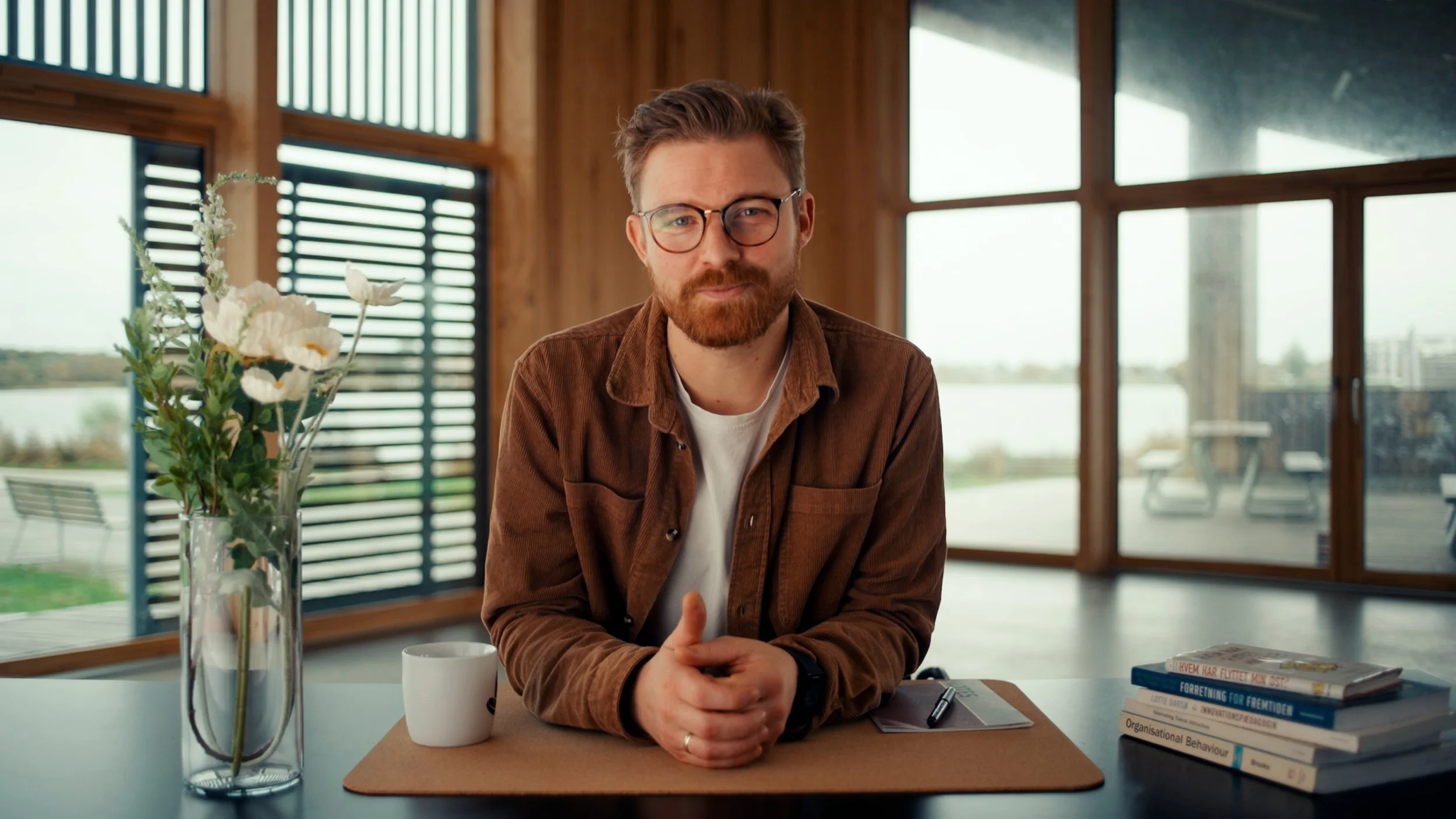 Stillgrab fra online masterclassen Rust din Virksomhed til fremtiden, billede af underviseren Buster der sidder ved et skrivebord i forløbets hero-skud. Tøj, baggrund og hår i varme jordtoner.