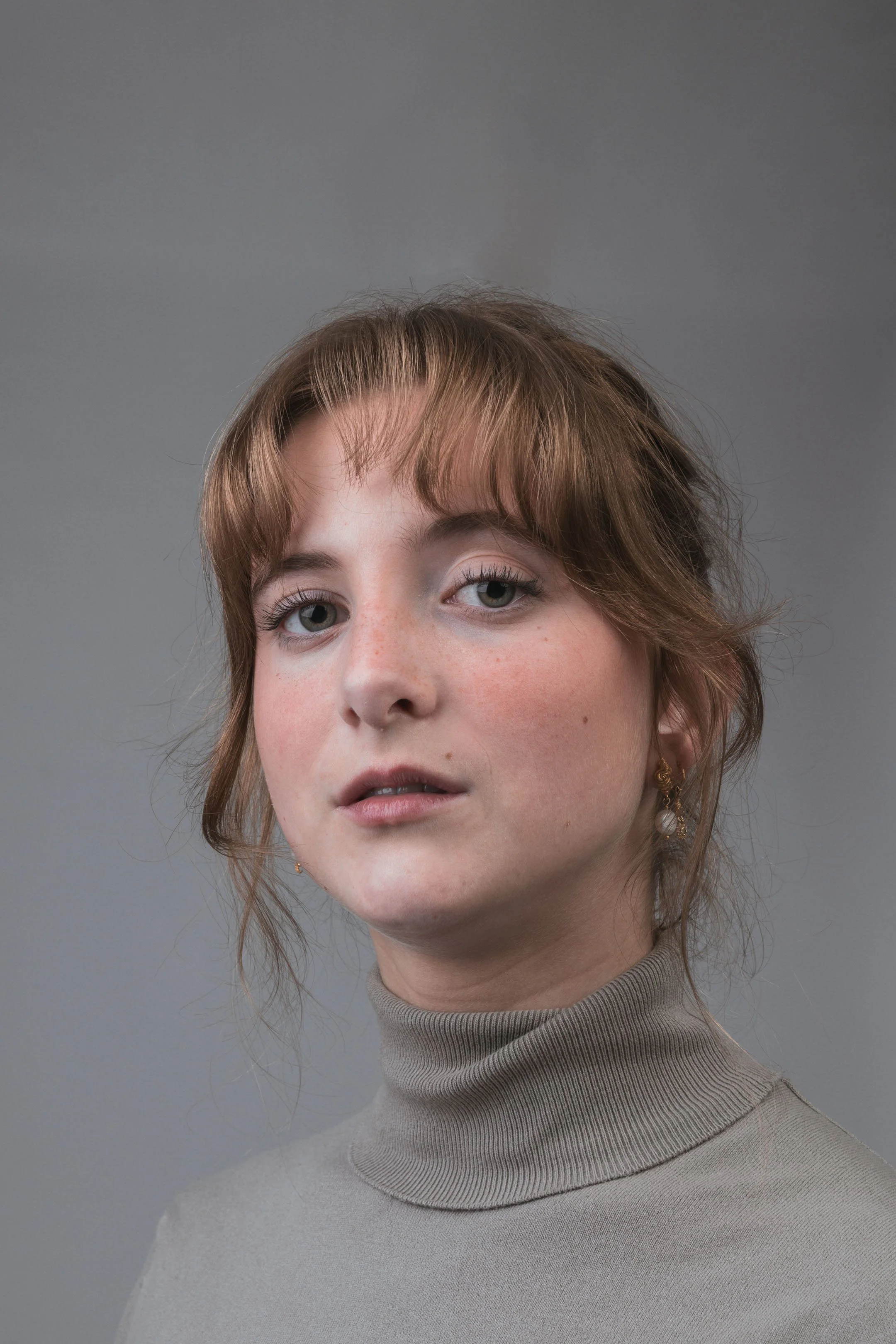 Portræt af ung kvinde med rødt hår med et stærkt blik, i grå turtleneck på grå baggrund - Studiesetting