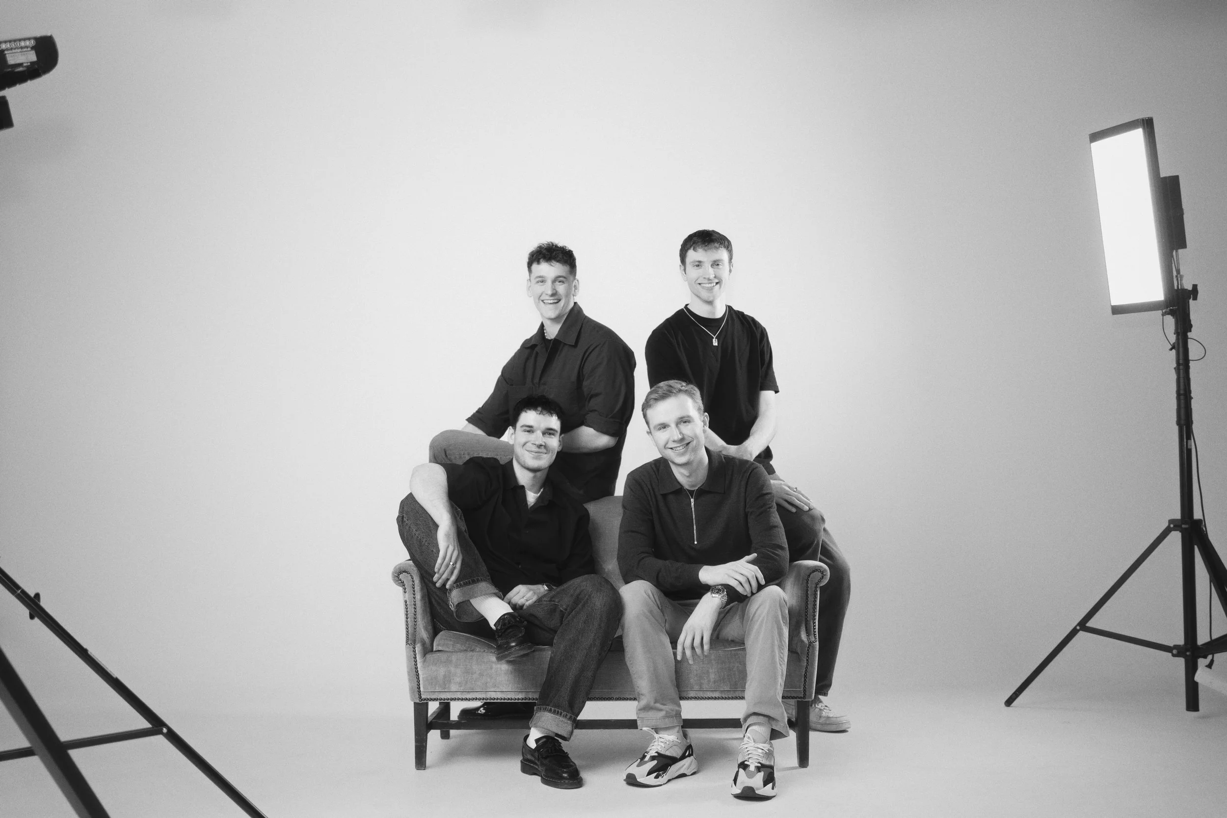 Gruppebillede af stifterne i et Film- & Reklameproduktionsselskab. Smilende i sofa. Sort/hvid Studiesetting.