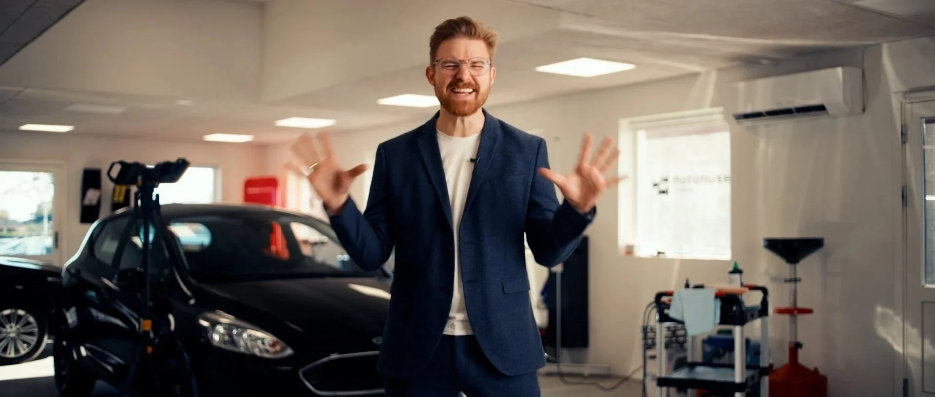 Stillgrab fra forløbet hvor Buster spiller en lidt for energisk bilsælger, dramatisk reklameagtig belysning og blåt jakkesæt.