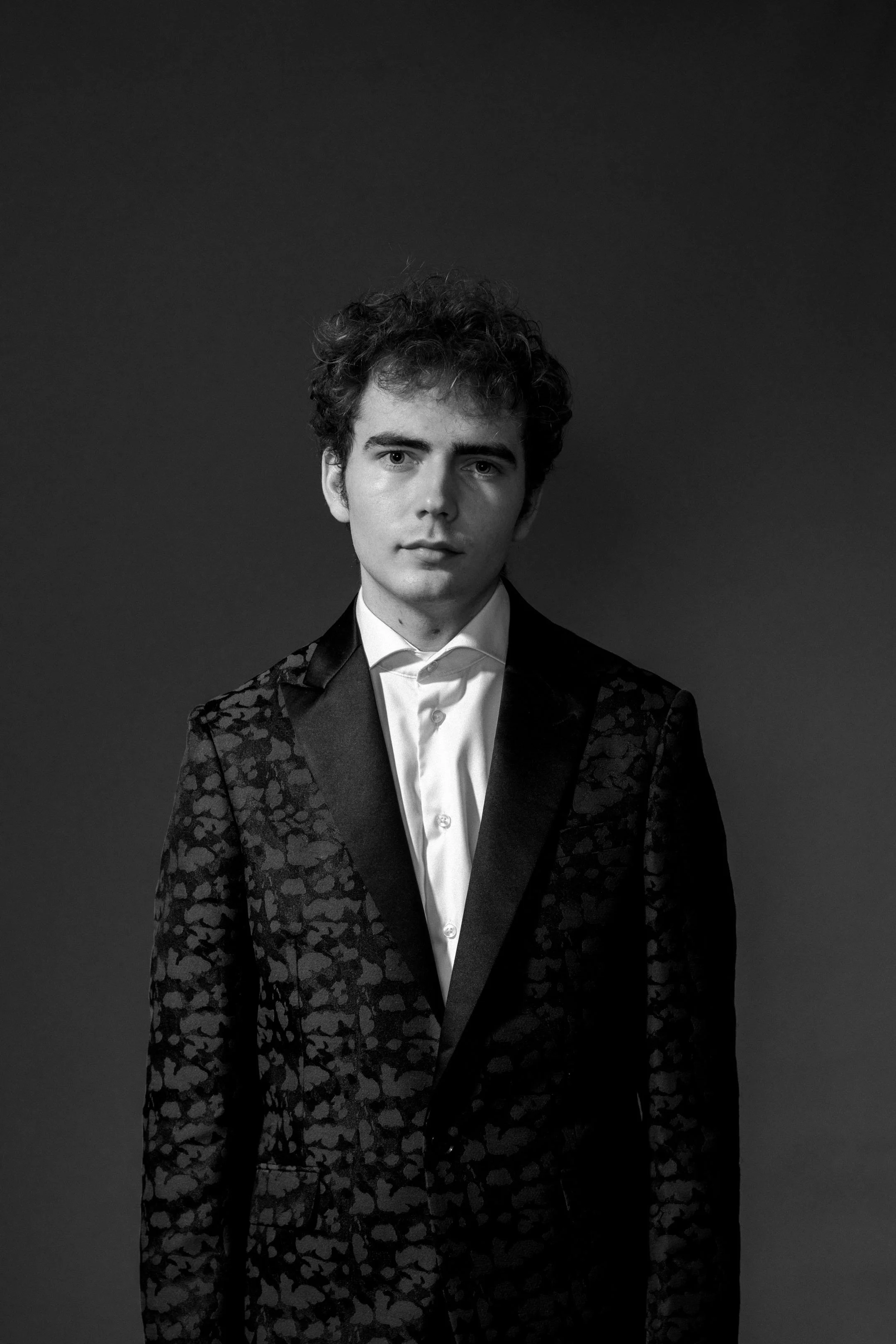 Portræt af ung operasanger der står med seriøst udtryk i sit jakkesæt. Dramatisk lys. Sort/hvid, Studiesetting.