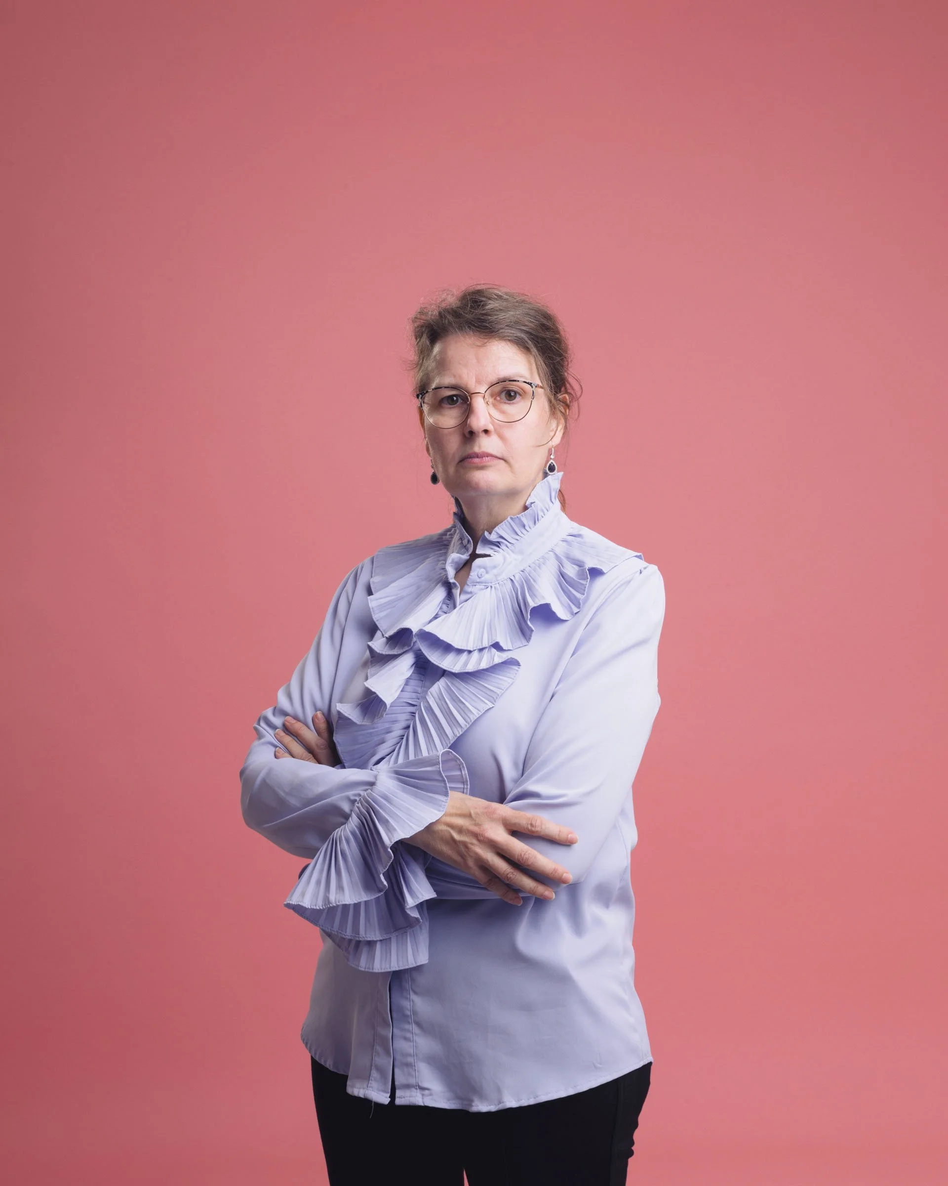 Portrætfoto af kvinde med seriøst men legende udtryk i lilla skjorte på lyserød baggrund - Studiesetting
