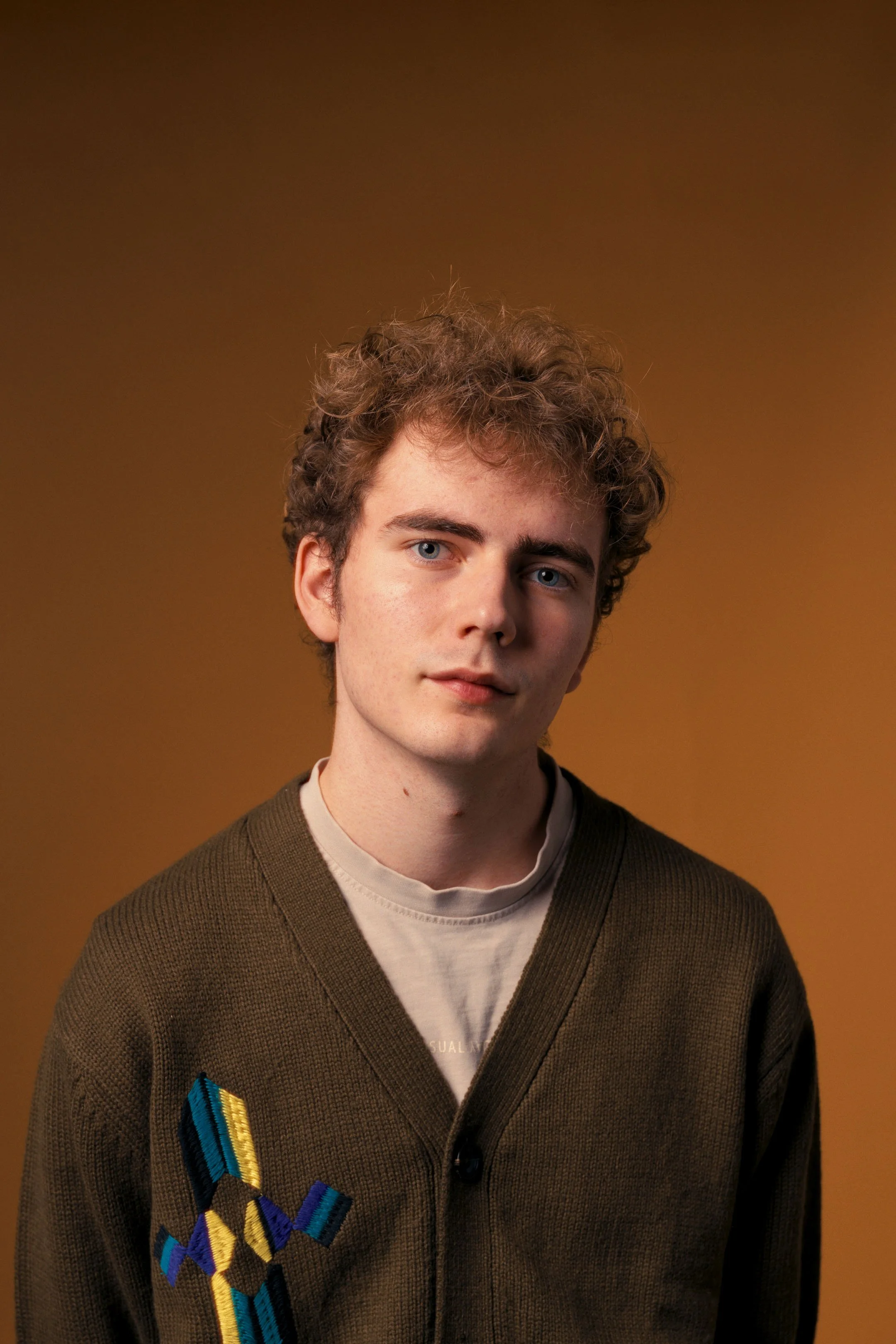 Portræt af eftertænksom ung mand i cardigan. Farverigt på orange baggrund. Studiesetting