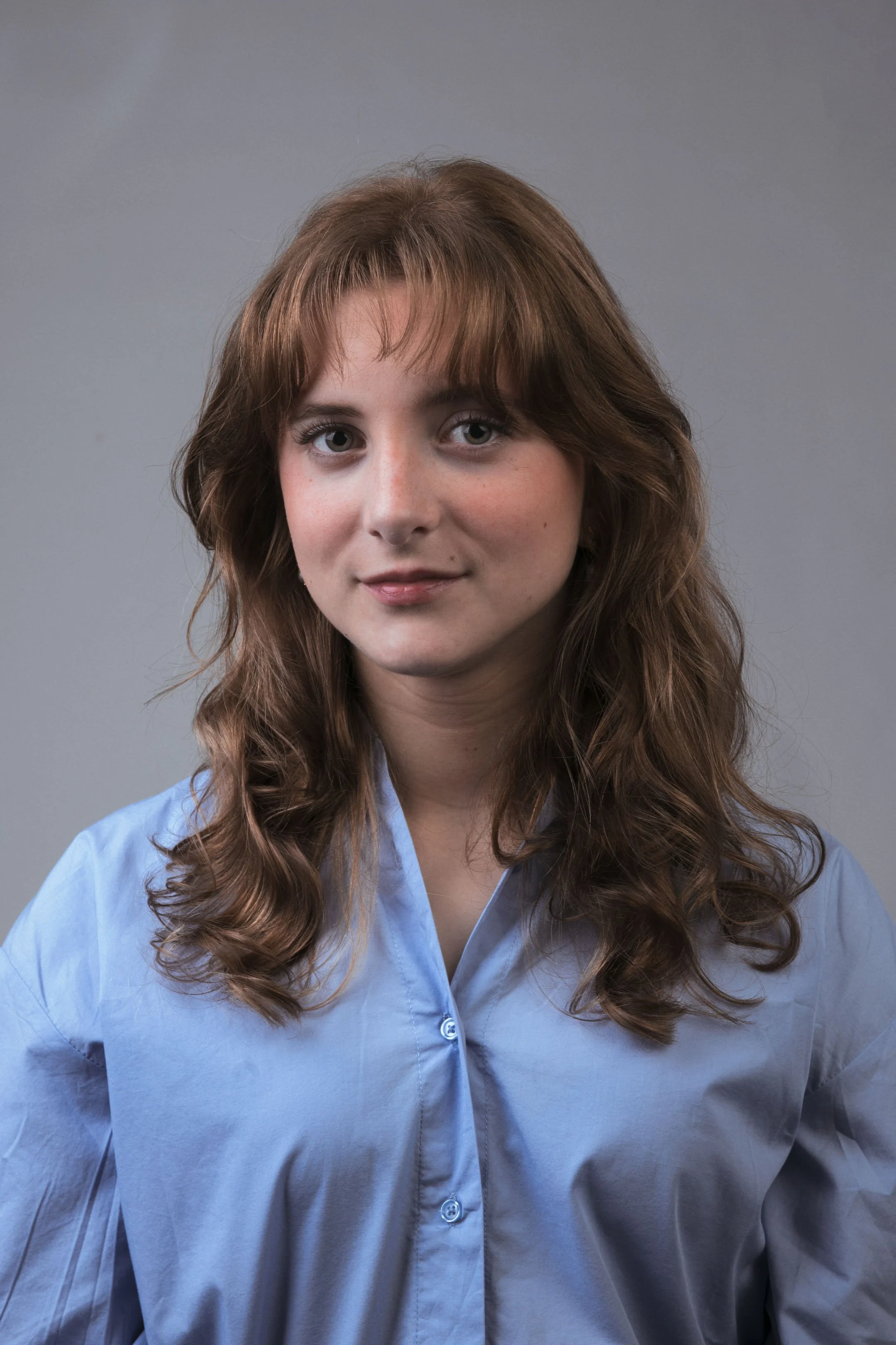 Portræt af ung kvinde med rødt hår med et stærkt blik, i blå skjorte på grå baggrund - Studiesetting