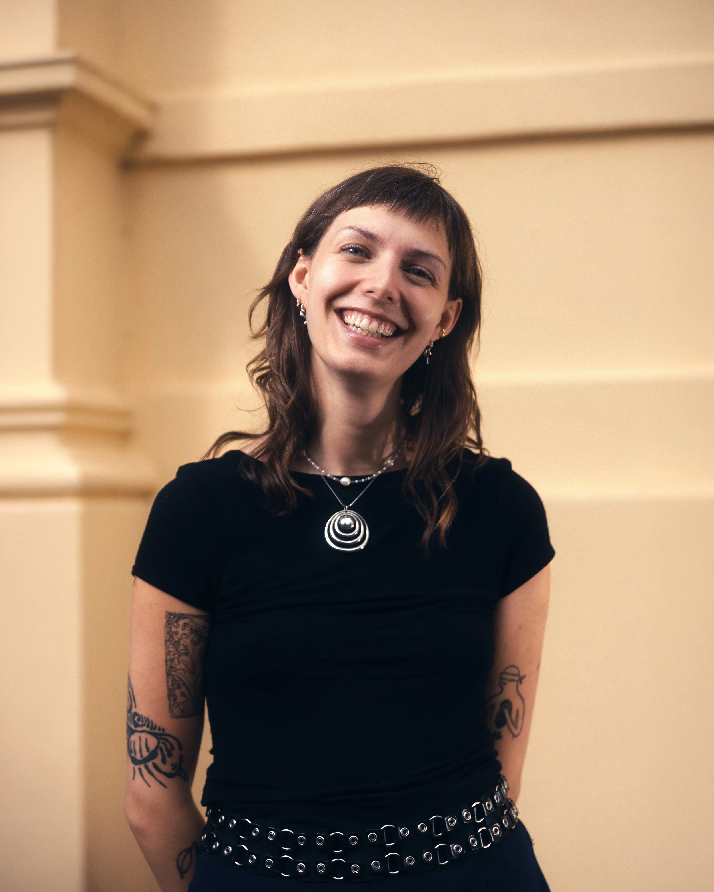 Erhversportræt af smilende kvindelig kulturformidler, med råt tøj og tatoveringer, udendørs.