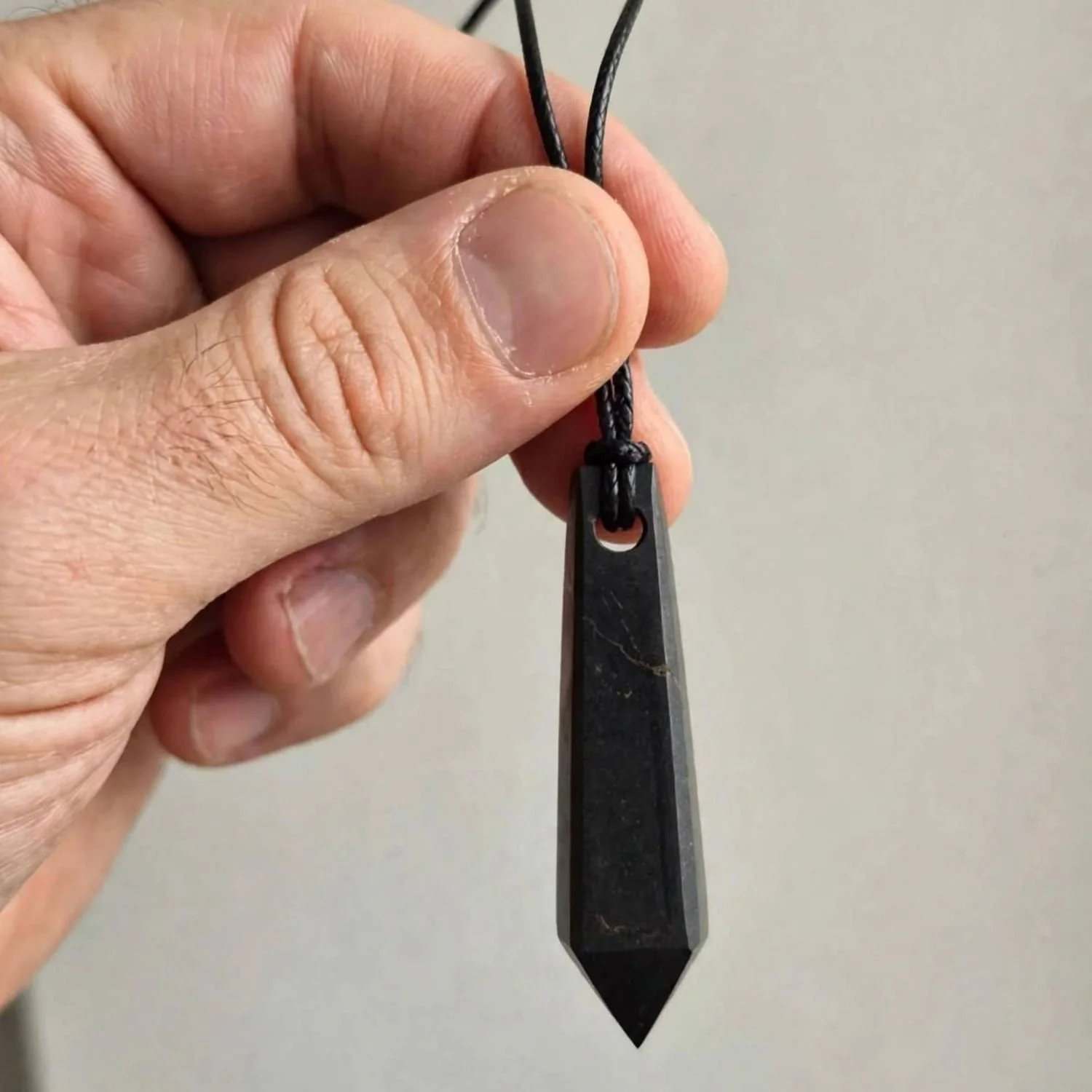 Schwarzer Schungit-Spitzenanhänger mit glatter Oberfläche und schwarzer Aufhängeschnur, in der Hand gehalten.