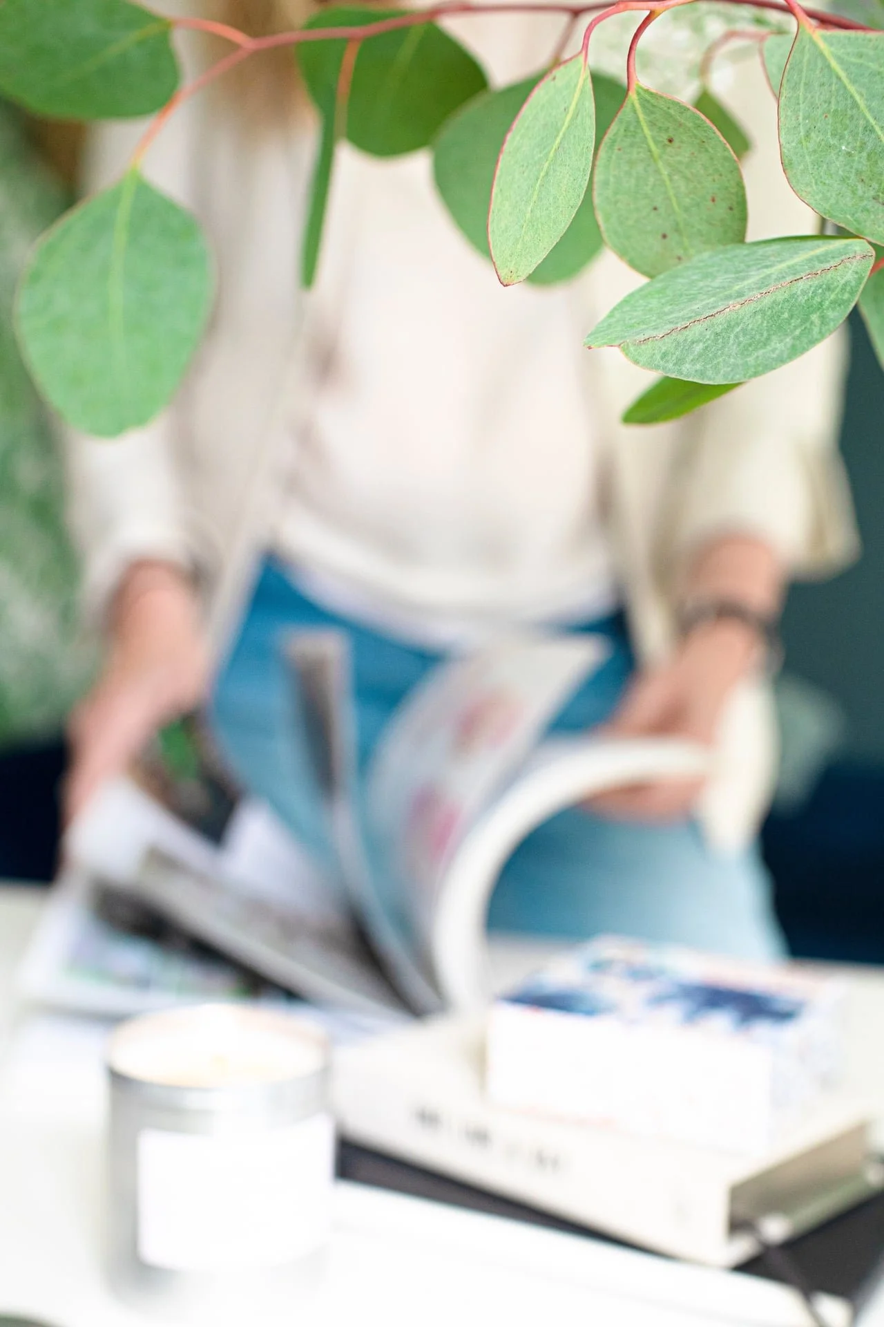 Close-up of green leaves with a person reading a magazine in the background, blurred.