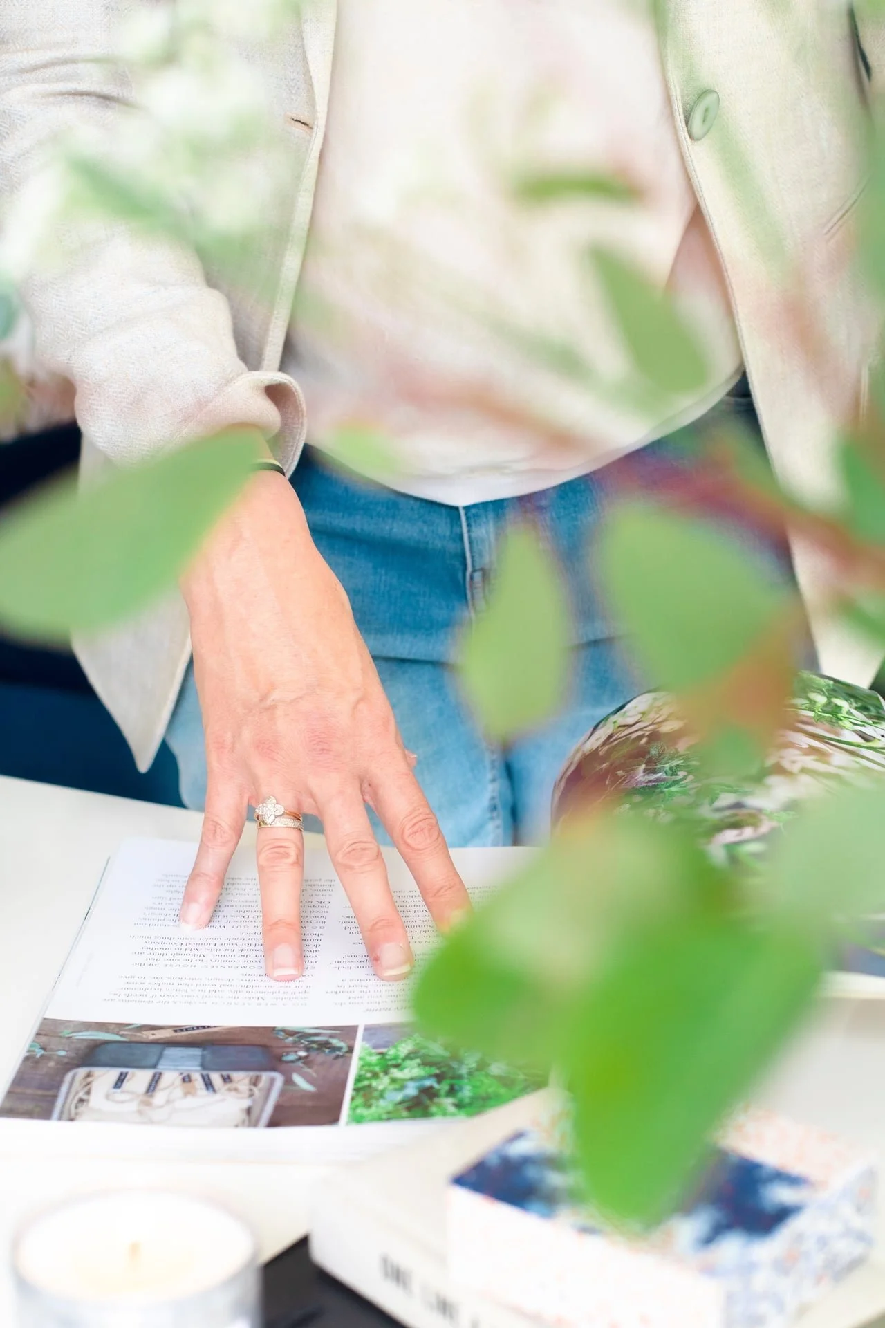 Person reading a magazine or brochure on a table, surrounded by green leaves and blurred objects.