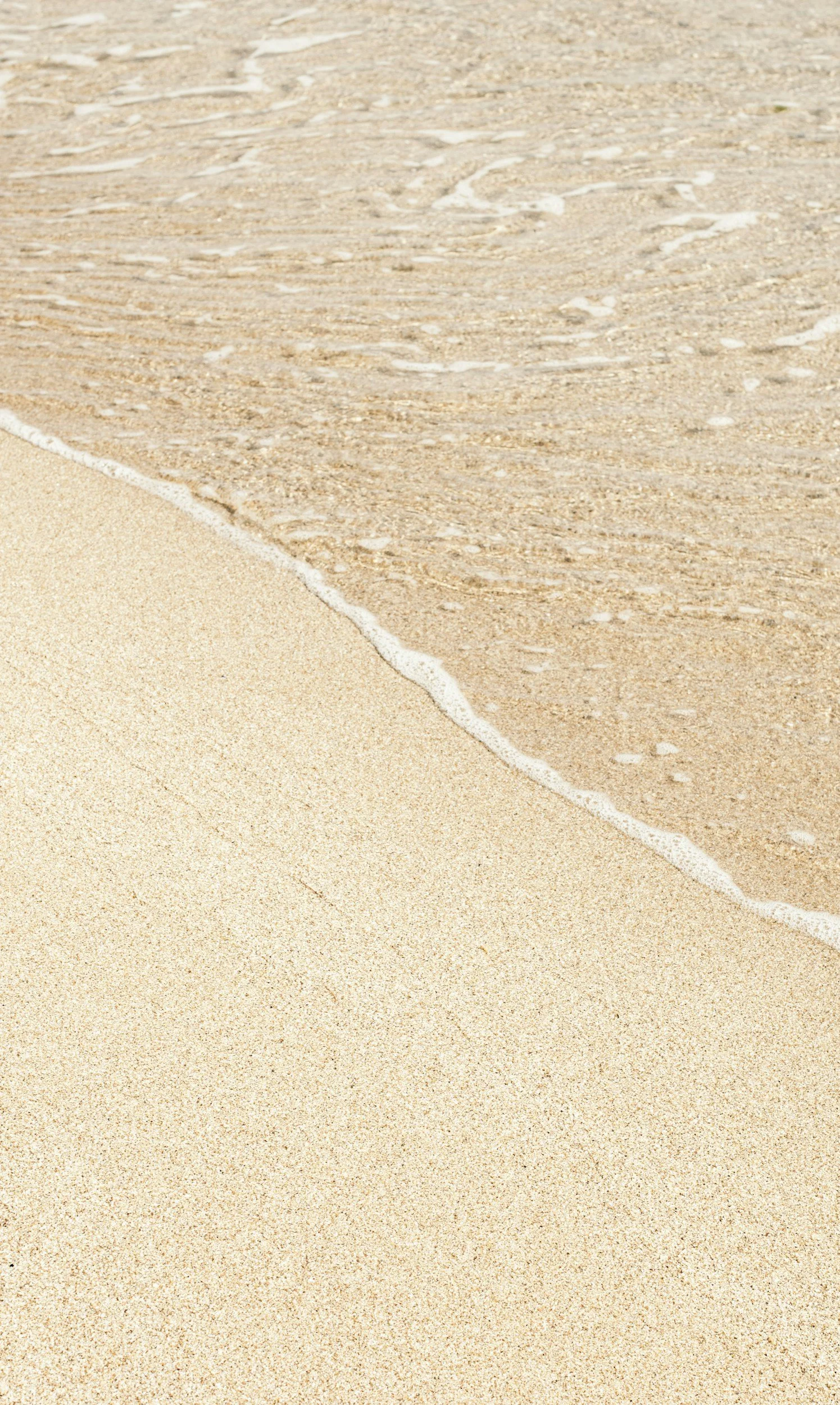 Close-up of a sandy beach with a gentle wave washing onto the shore.