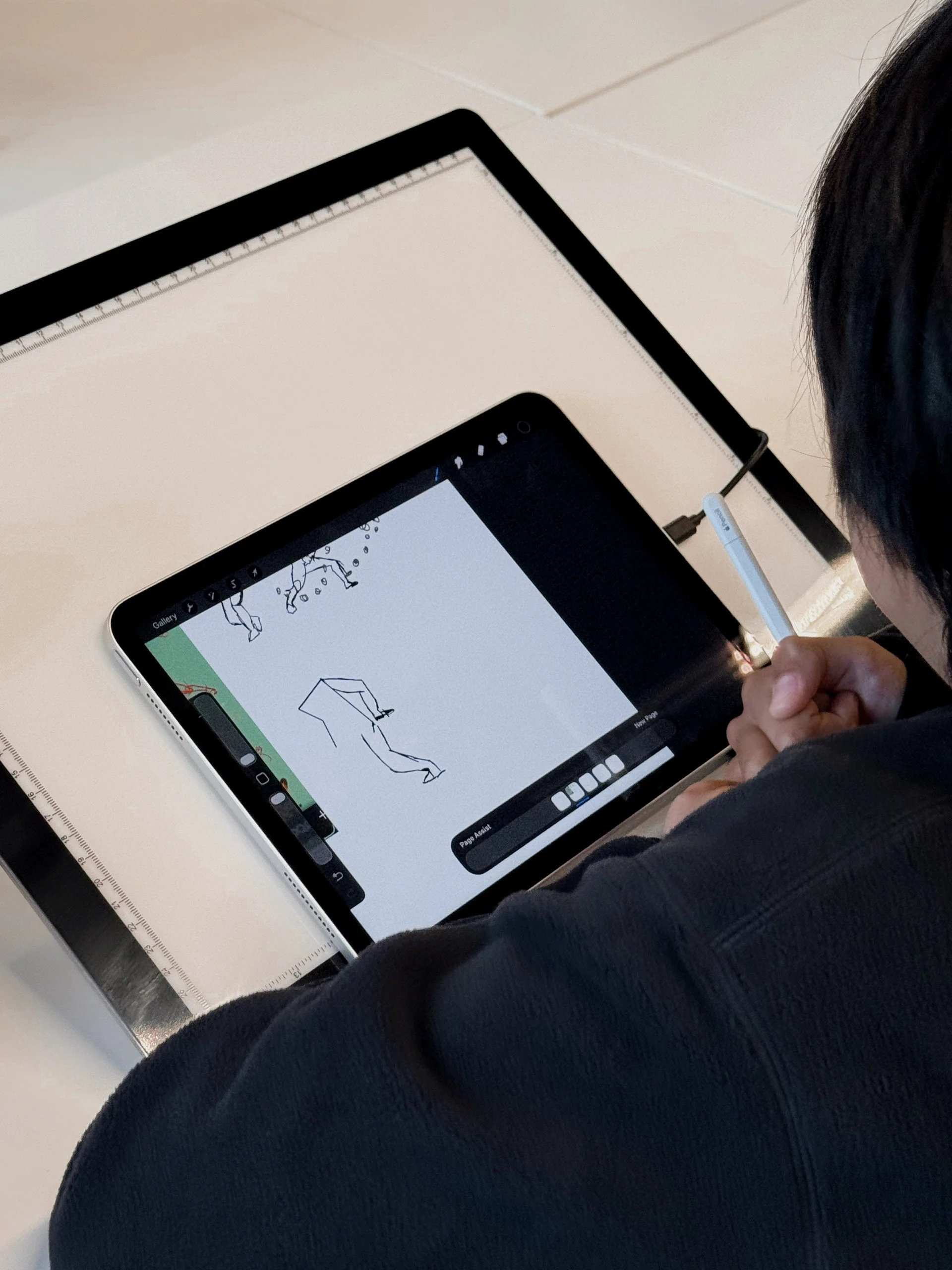 Person holding stylus drawing stick figures and objects on a digital tablet at a desk.