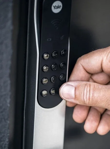 Person som trycker på en kodlåsknapp med siffrorna 1 till 9 på ett Yale-föremål.