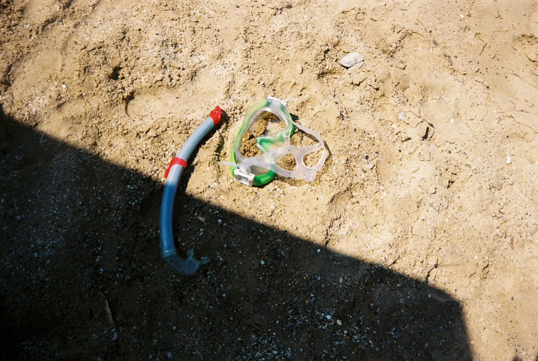 En svømmebrille og en snorkel ligger på sanden.