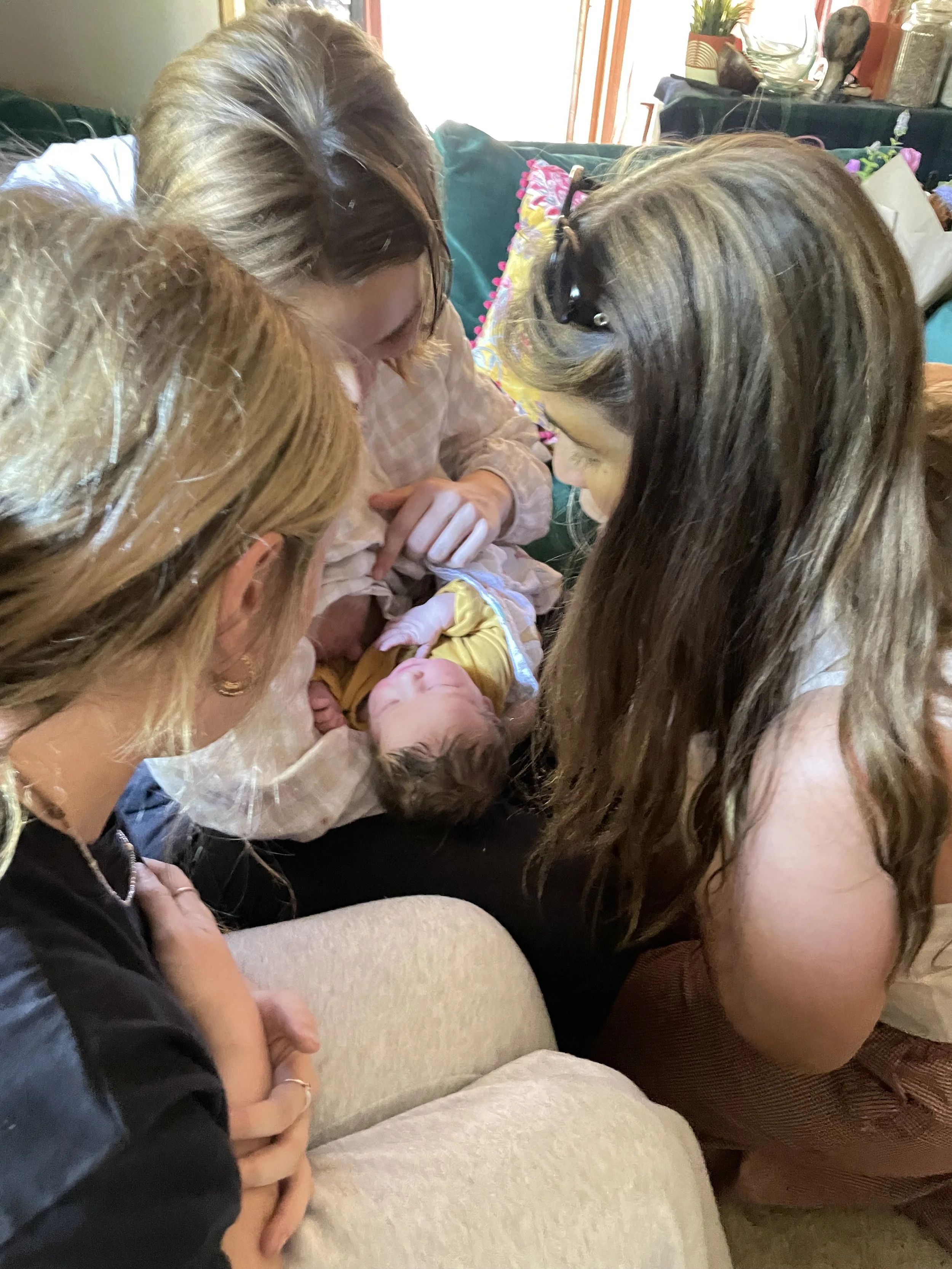 Multiple women gathered around a newborn baby, appearing to be bonding or delivering the baby, in a cozy, well-lit room.