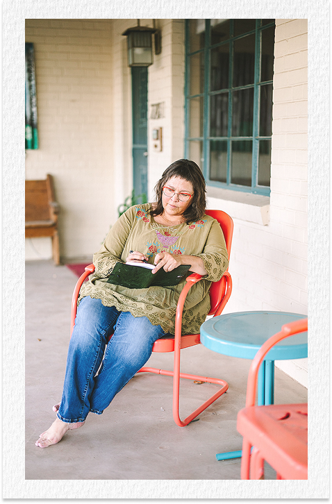 Woman sitting outside on a porch, reading or using a tablet.
