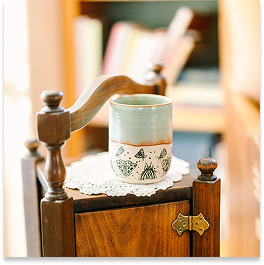 A ceramic mug on a wooden chair with a lace doily, in a cozy room.