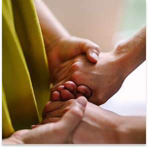 Two people holding hands, one supporting the other's hand in a caring manner.