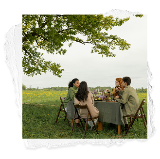 Four people having a meal at a table outdoors under a large tree