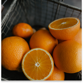 Fresh oranges, some whole and one halved, in a plastic basket.