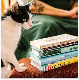 Black and white cat with yellow eyes on a couch next to a stack of health and wellness books.