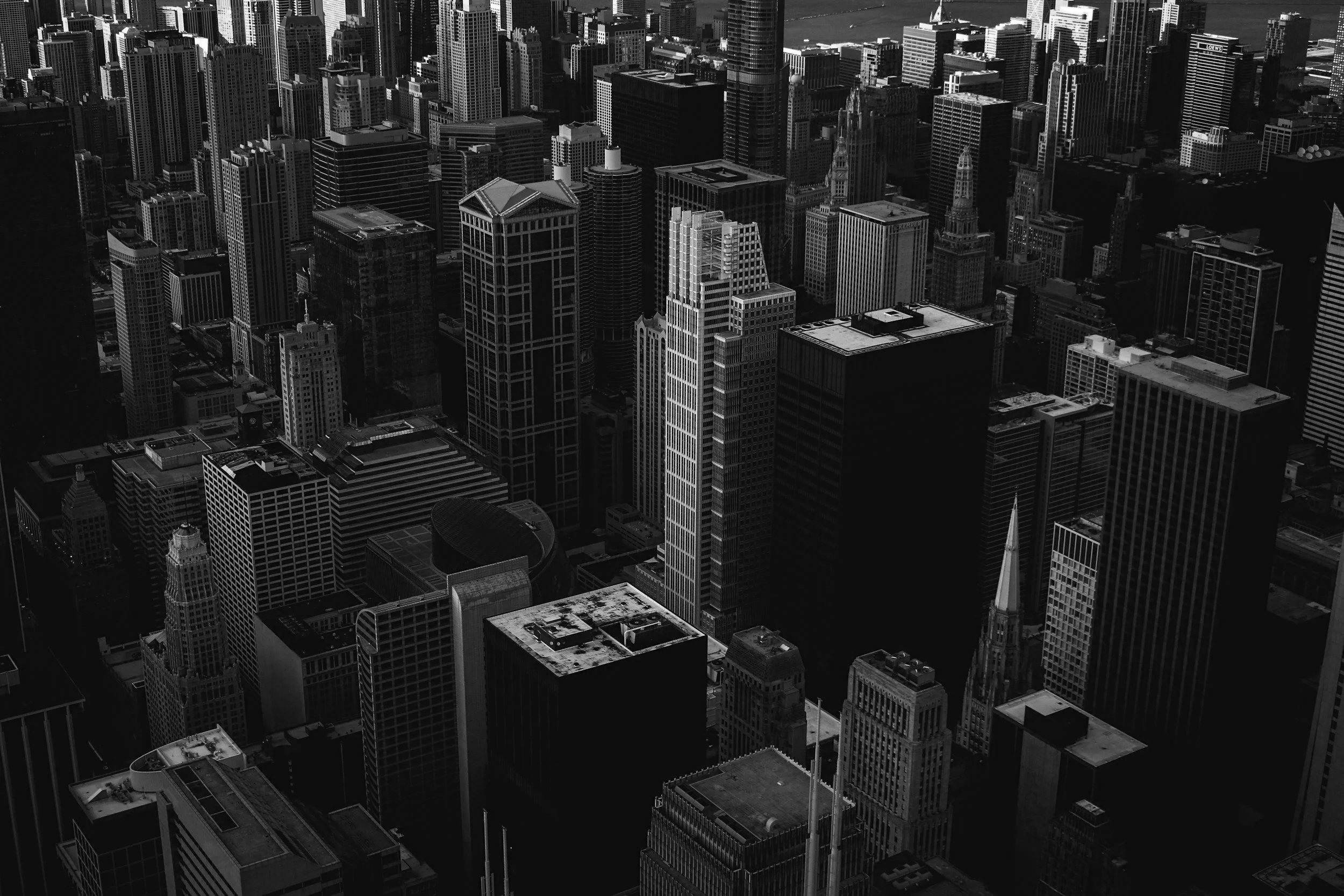 A black and white aerial view of a dense downtown cityscape with numerous tall skyscrapers and office buildings.