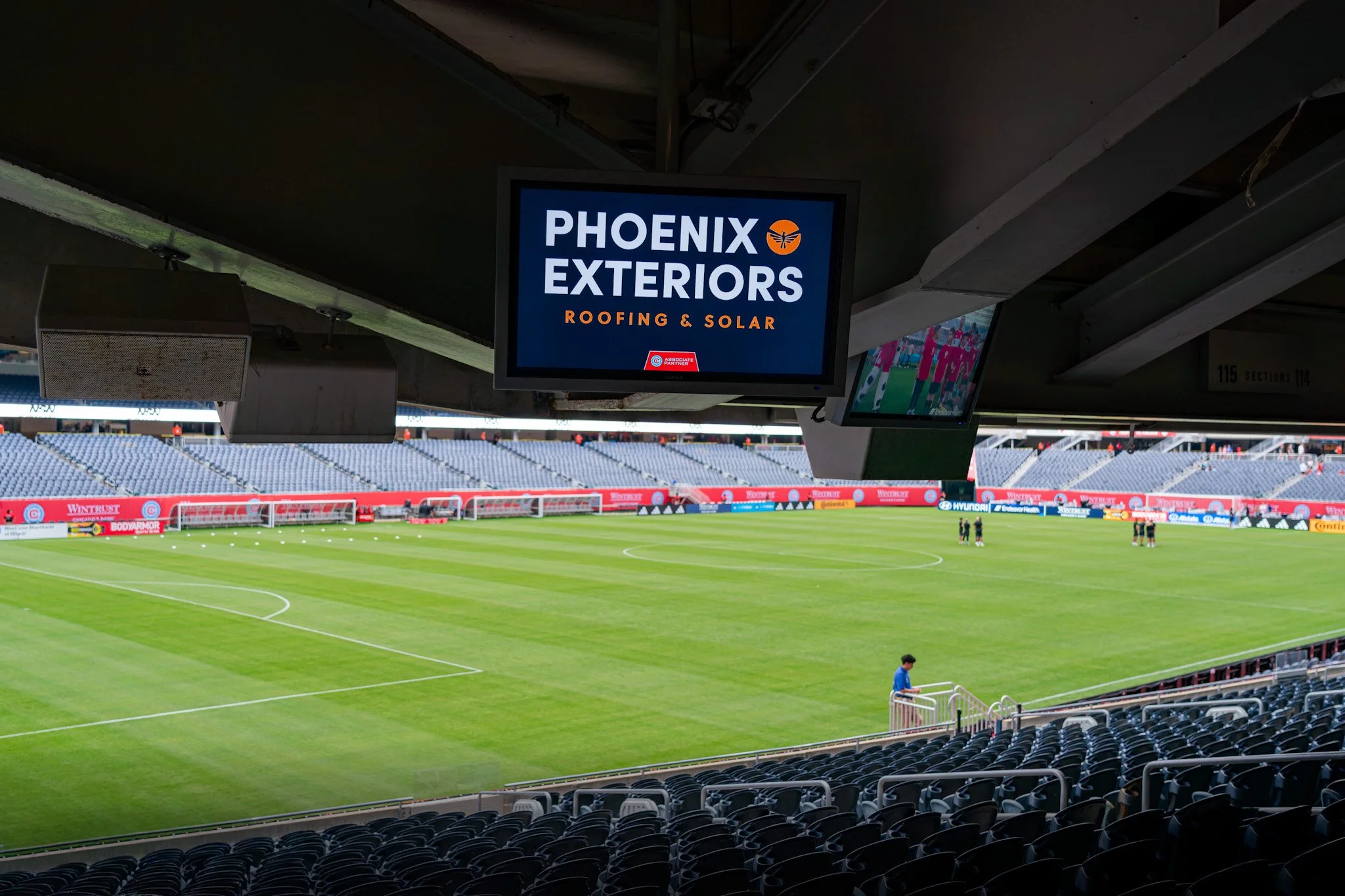 Empty soccer stadium with green field, empty seats, and large screens displaying advertisements and a team march.