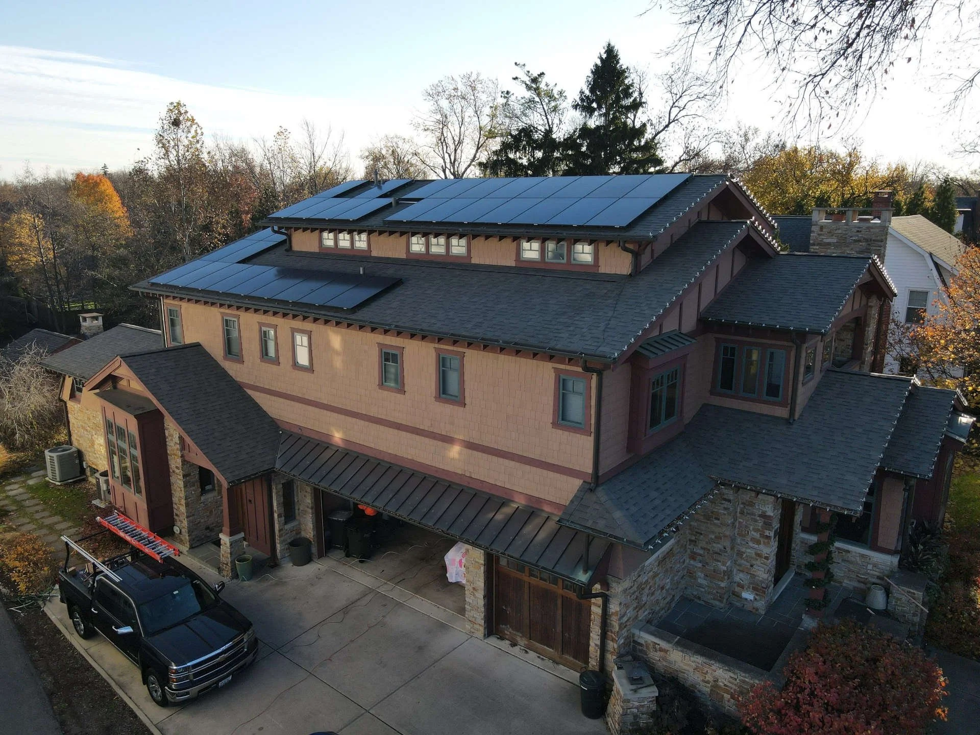 A large multi-story house with solar panels on the roof, surrounded by trees with fall foliage.