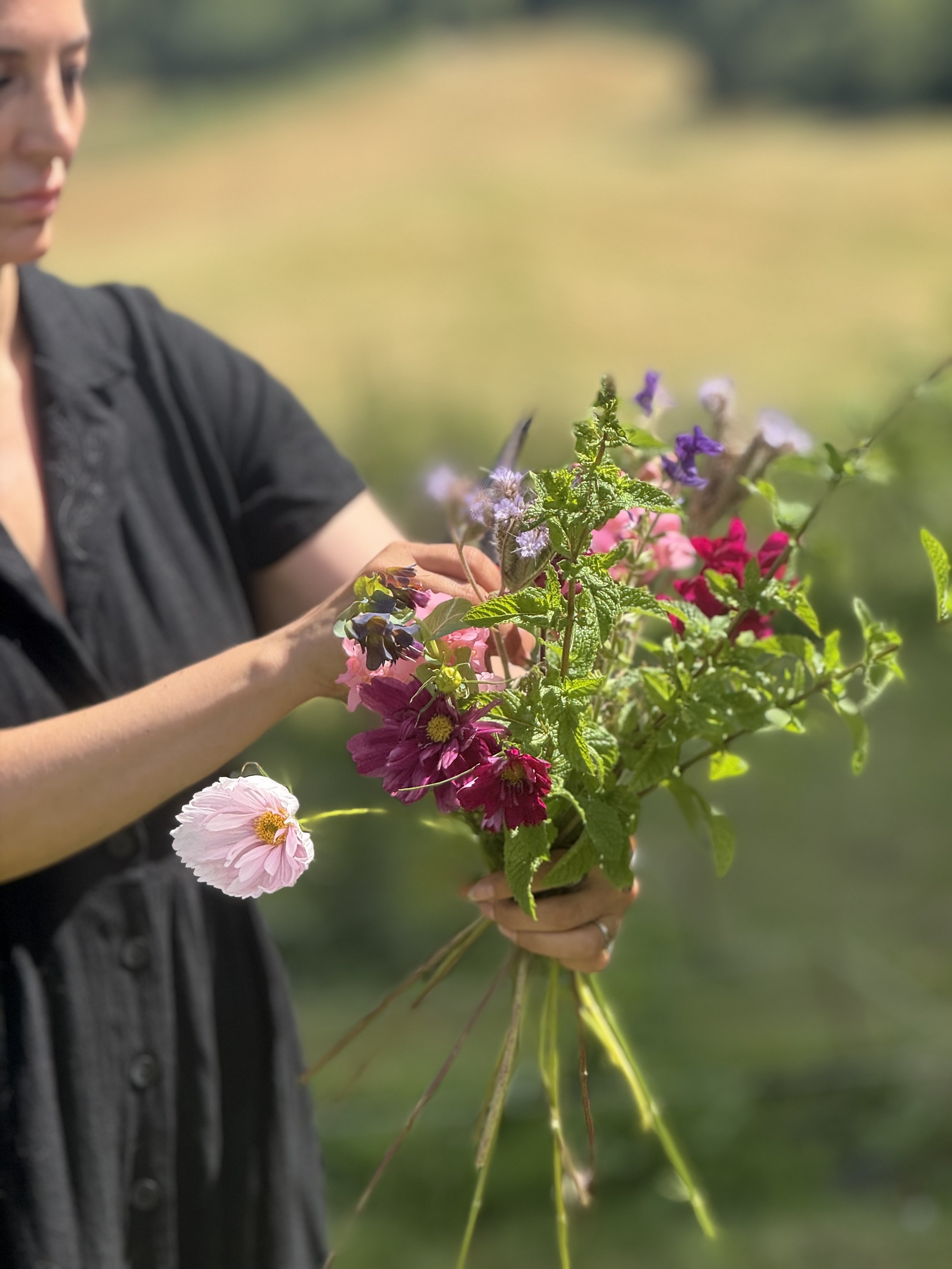 A person holding a bouquet of mixed colorful flowers outdoors, with a blurred green background.
