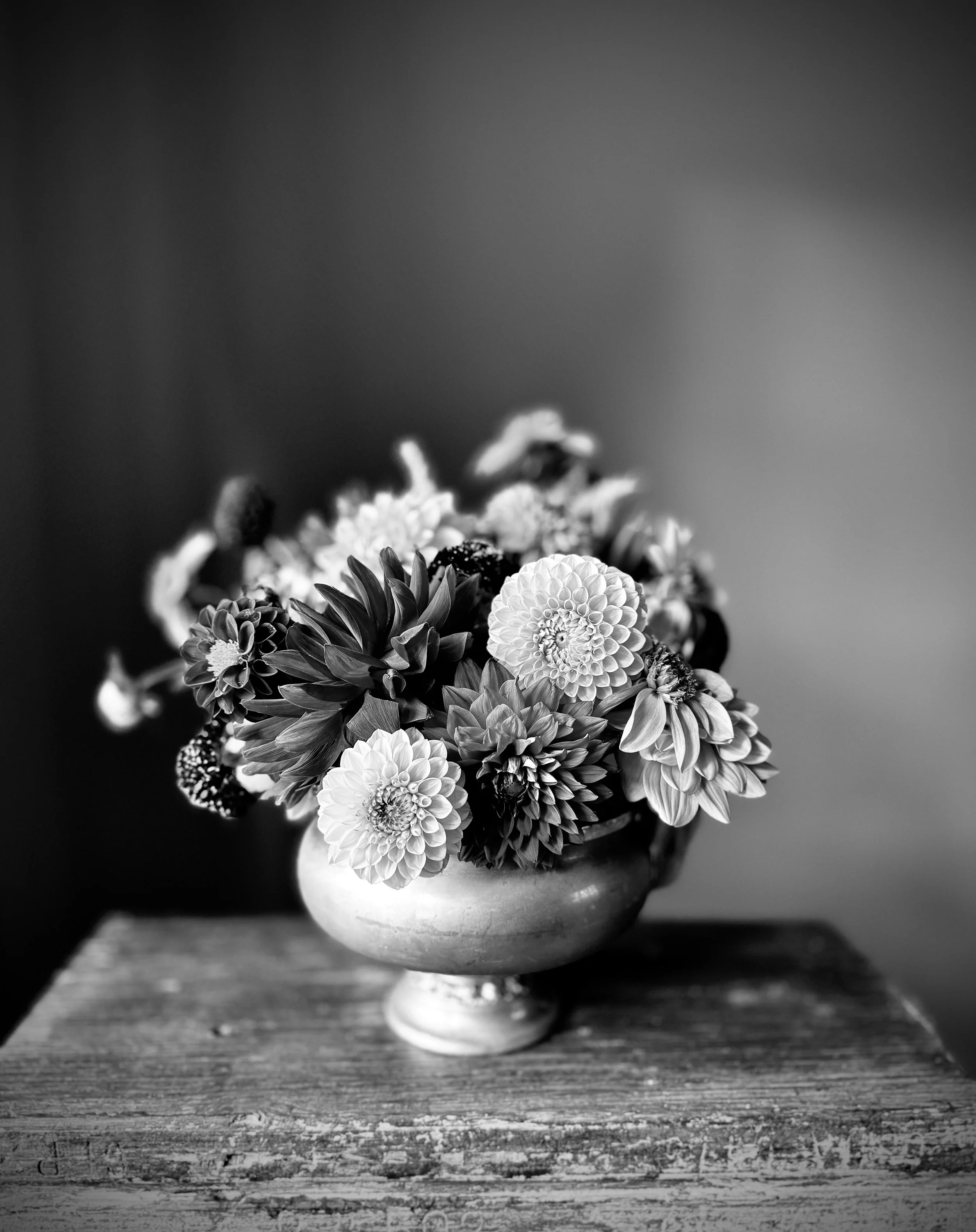 Black and white photo of a flower bouquet in a vase on a wooden surface.