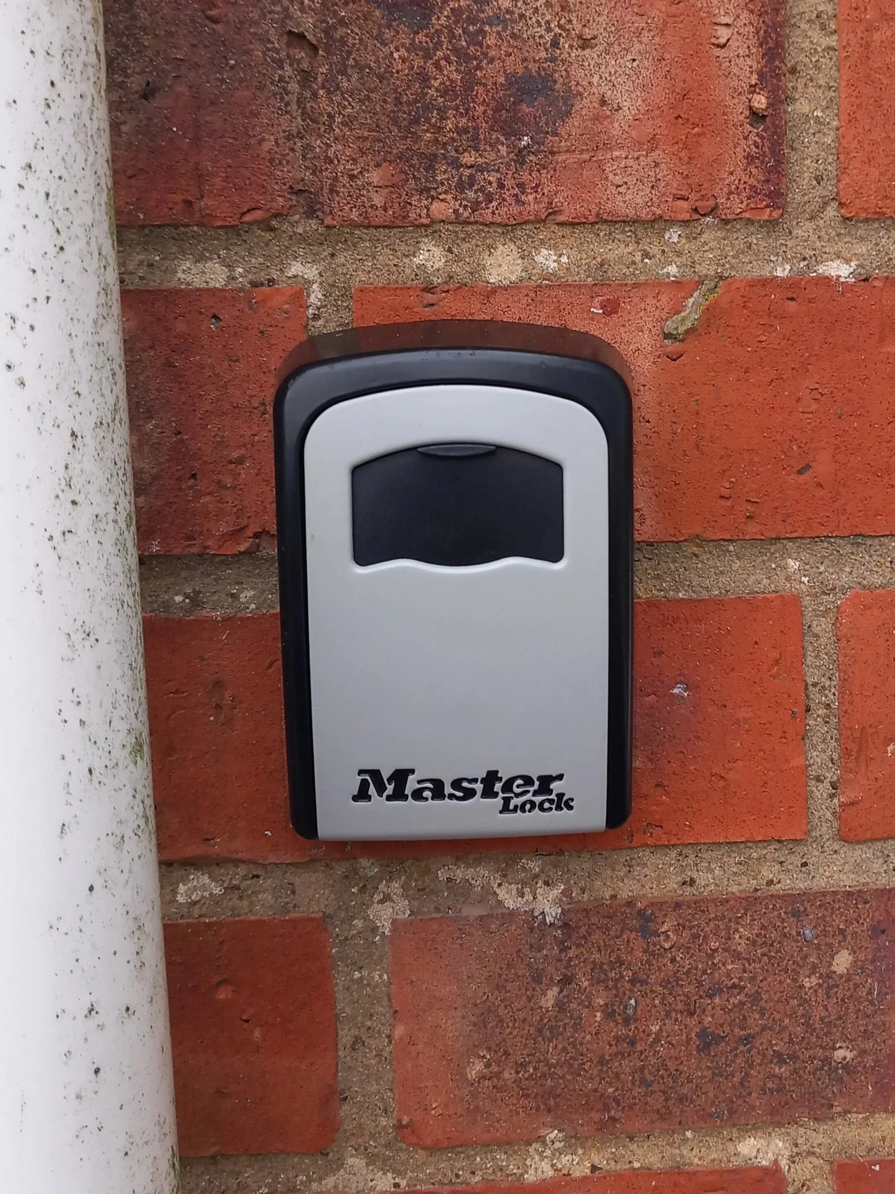 A key safe mounted on a brick wall, next to a rainwater pipe