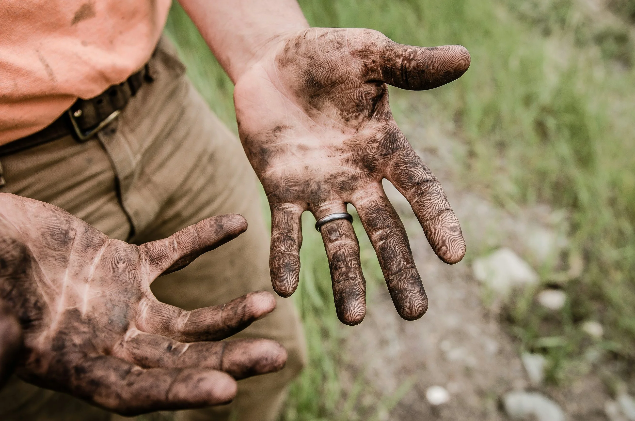 Person with muddy hands, wearing a ring, showing dirt-covered fingers in an outdoor setting.