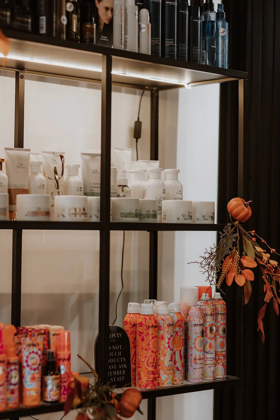 Shelf with various hair products, including bottles and containers, some with colourful floral designs, decorated with autumn leaves and small pumpkins.