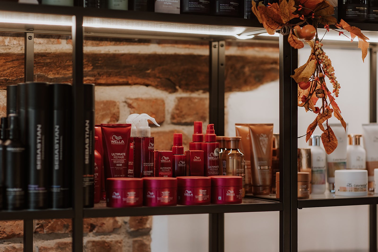 Various haircare products on black metal shelves against a brick wall, with an autumn-themed decoration hanging on the side.