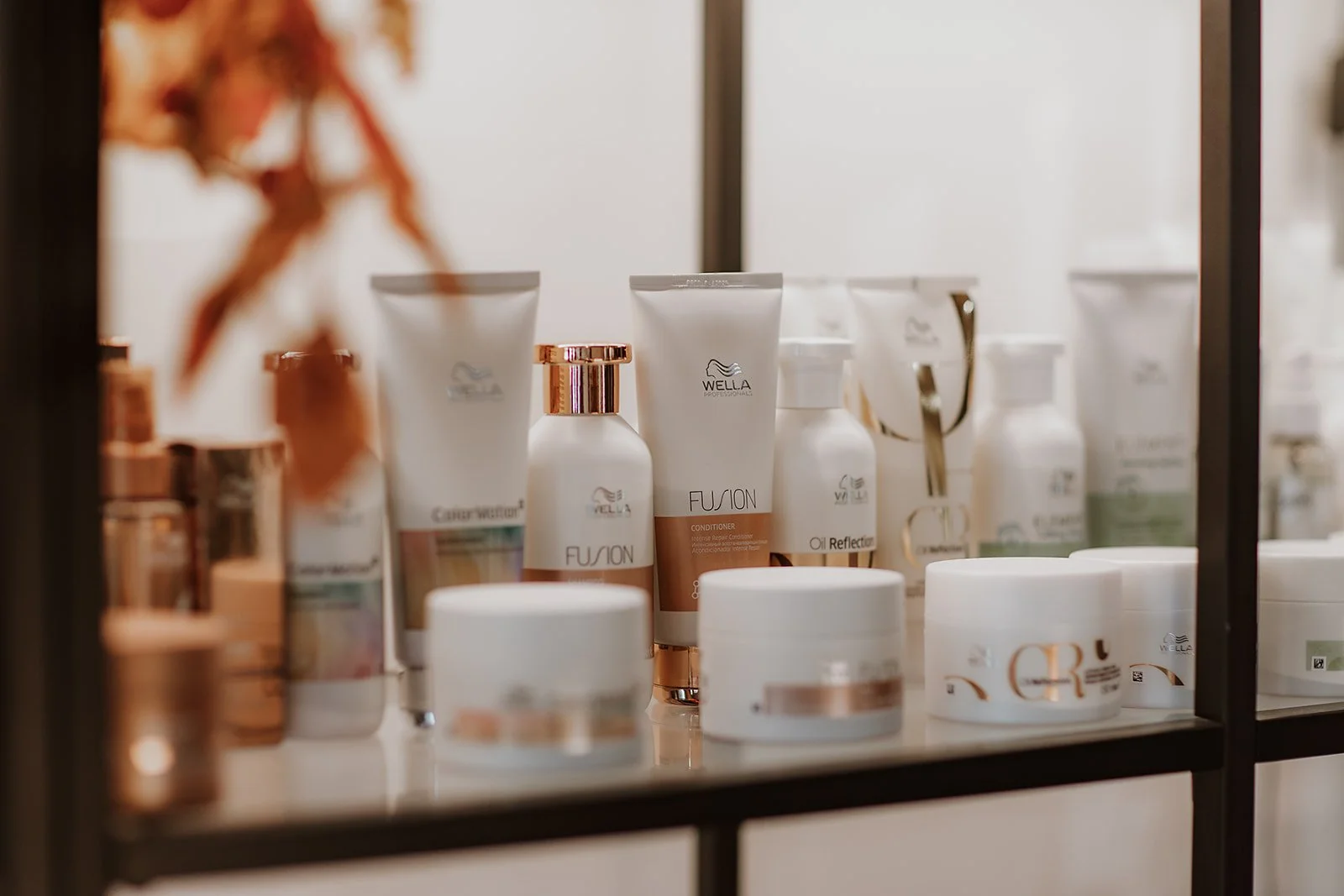 A display of various Wella hair care and styling products in white, copper, and green packaging on a glass shelf, reflected in a mirror.