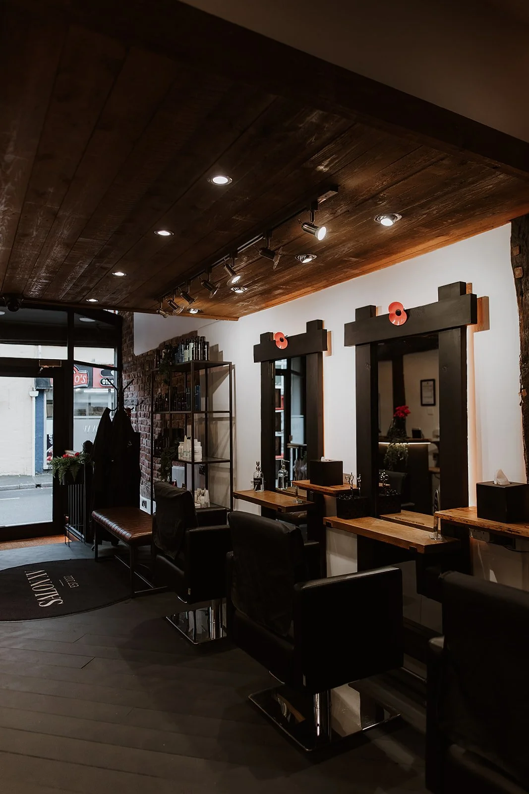 Interior of Salon XV in Oswestry with black chairs, wooden styling stations, mirrors, and a brick and white wall background.