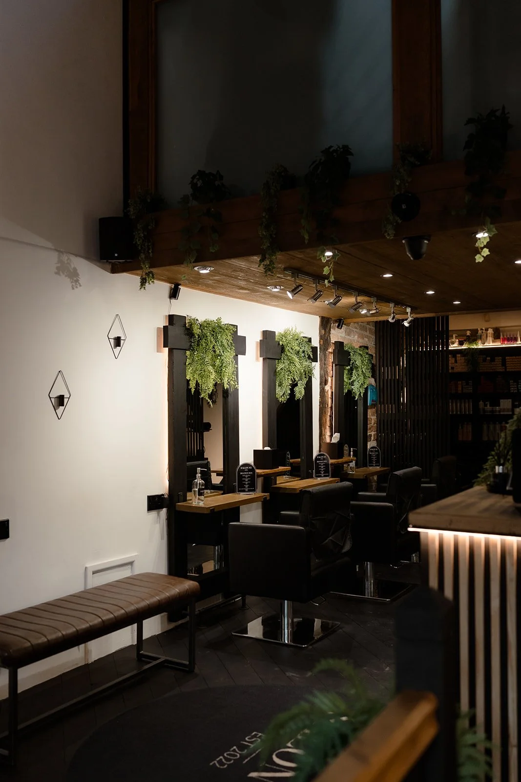 Interior of a modern salon with black chairs, wooden mirrors with plants, and ambient lighting.