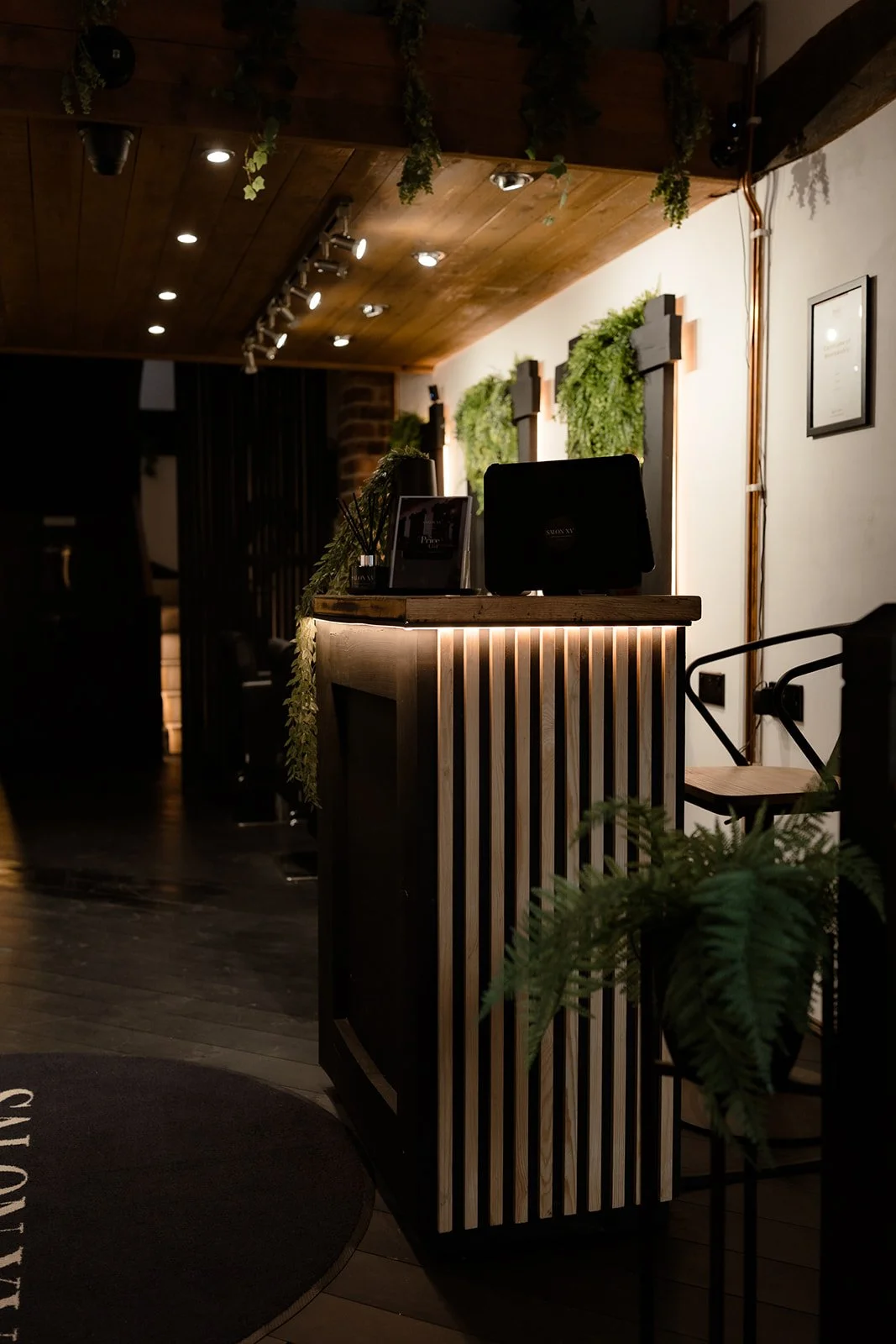 Reception desk with monitor, framed photo, and decorative plants, illuminated with warm lighting in a cozy, modern interior