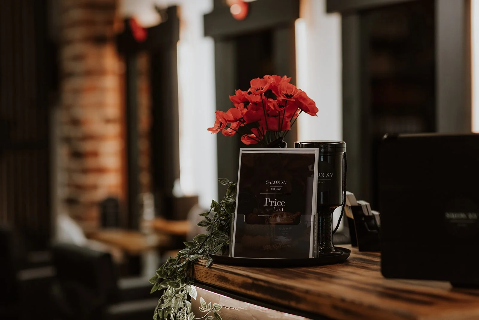 The reception desk at Salon XV on Beatrice Street in Oswestry with a vase of red flowers and a price list.