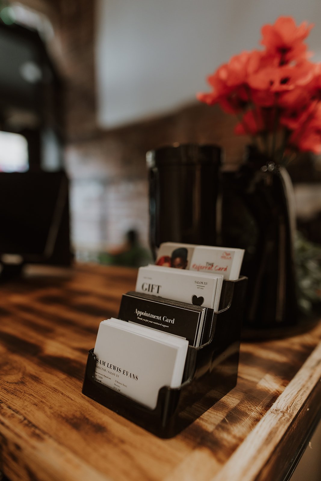 Business card holder with various cards on a wooden table, background includes a black vase with red flowers. 